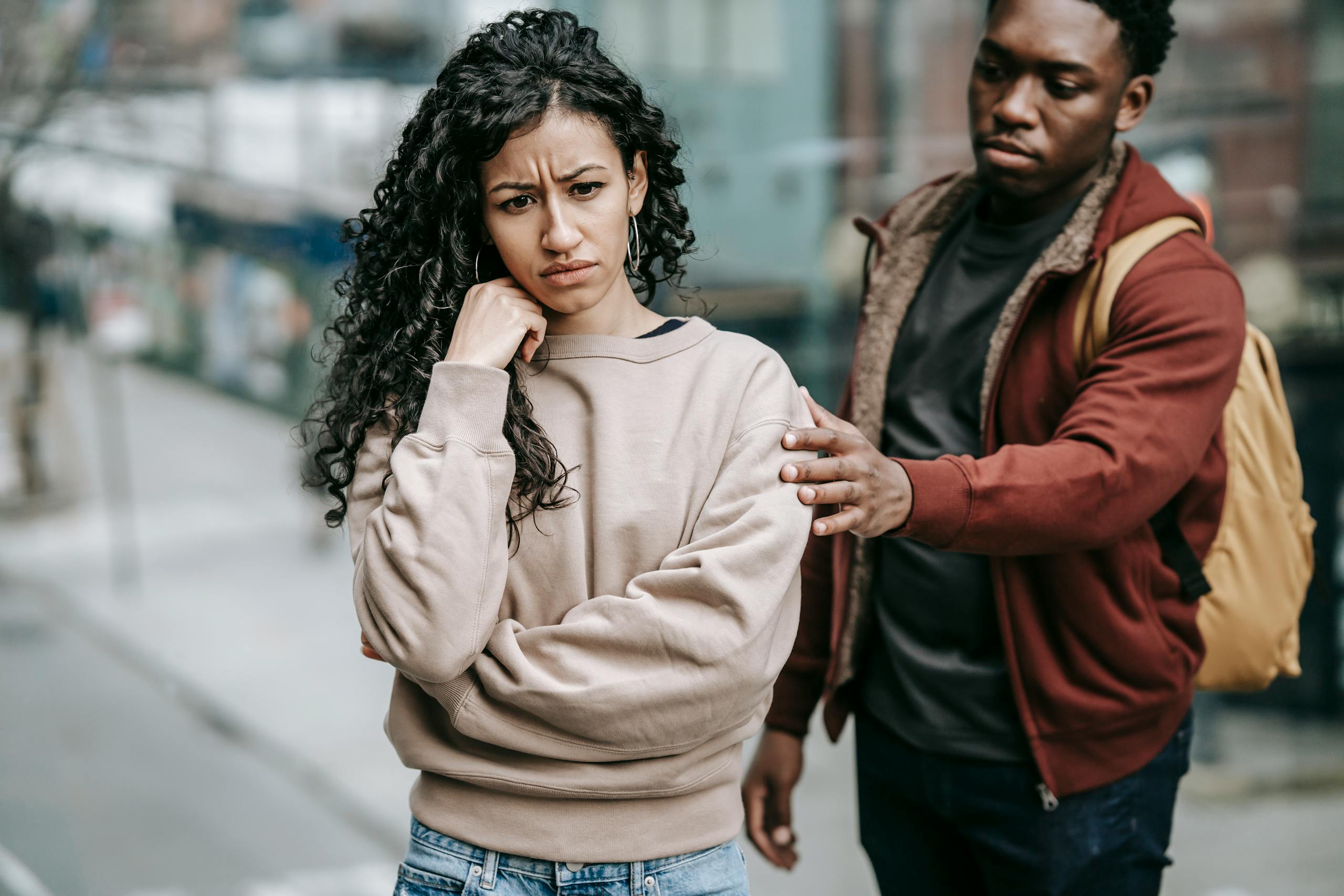 Sad young multiethnic couple in casual clothes standing in city street while having disagreement in daylight