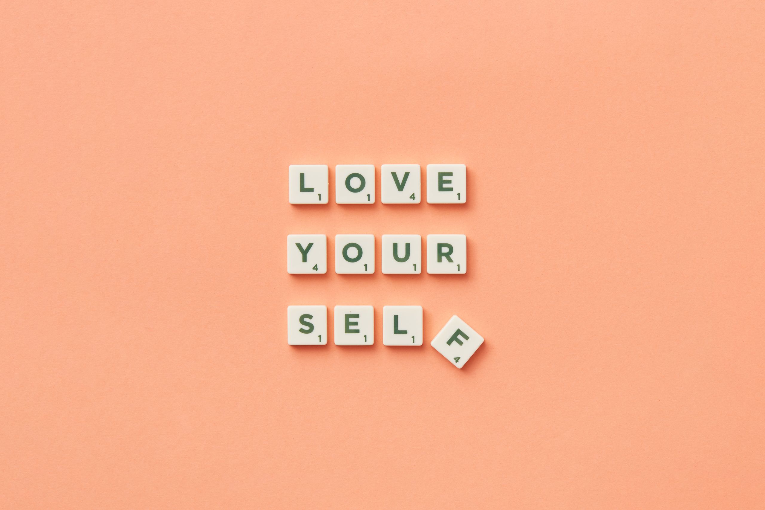 Scrabble tiles spelling 'Love Yourself' on a peach background, inspiring self-care.