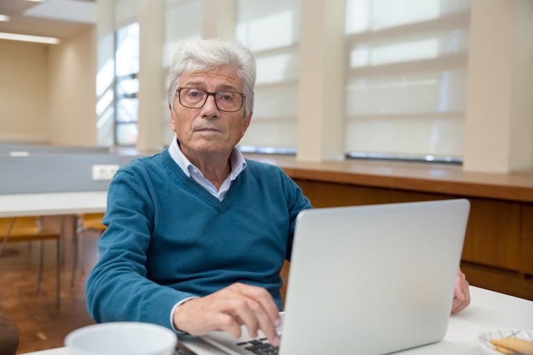 Senior man working remotely on a laptop in an office environment.