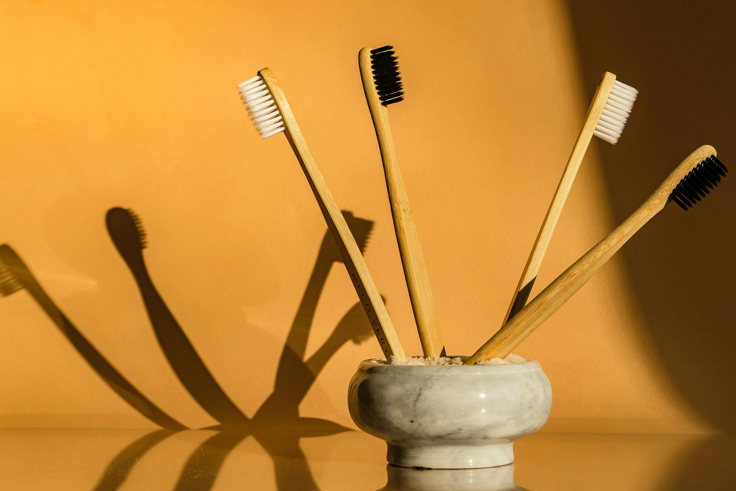 Set of bamboo toothbrushes in ceramic holder against orange backdrop, showcasing eco-friendly dental care.