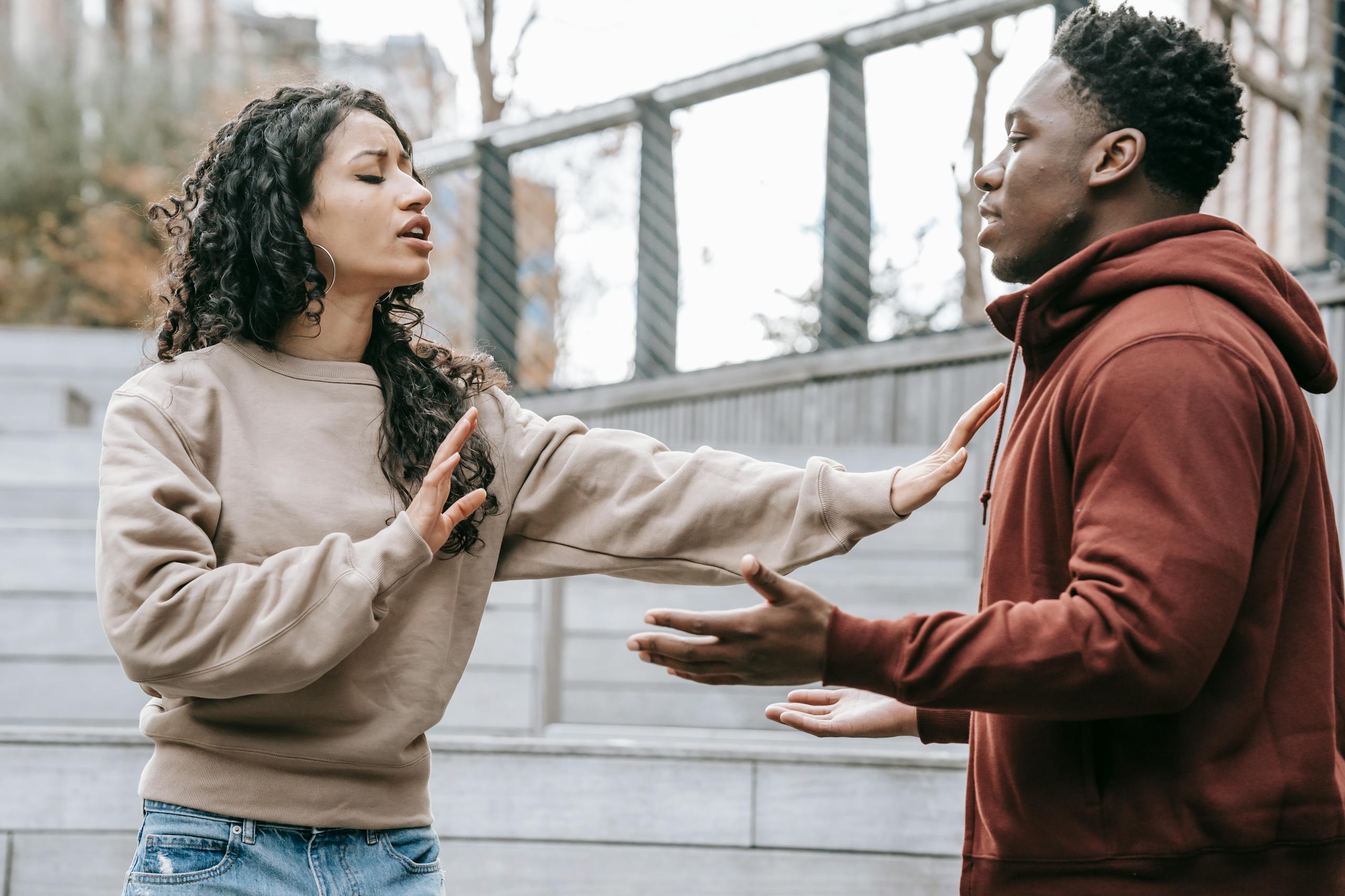 Side view of ethnic woman with outstretched arms trying to stop African American man while breaking up on street in city