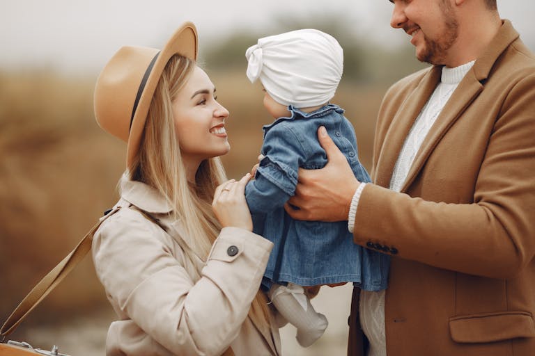 Side view of positive stylish young mother and father playing with adorable little daughter outside in autumn day