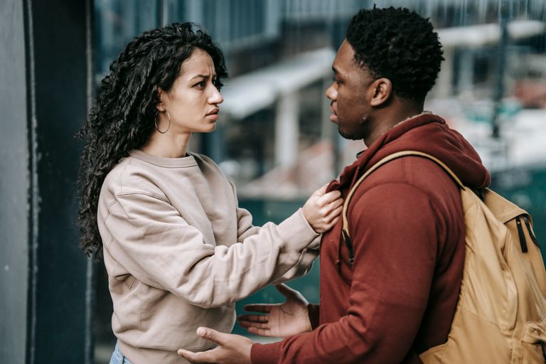 Side view of young unhappy diverse couple in casual clothes standing together and looking at each other