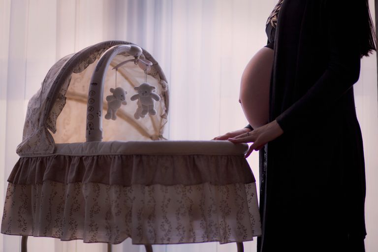 Silhouette of a pregnant woman next to a baby cradle in a softly lit room.