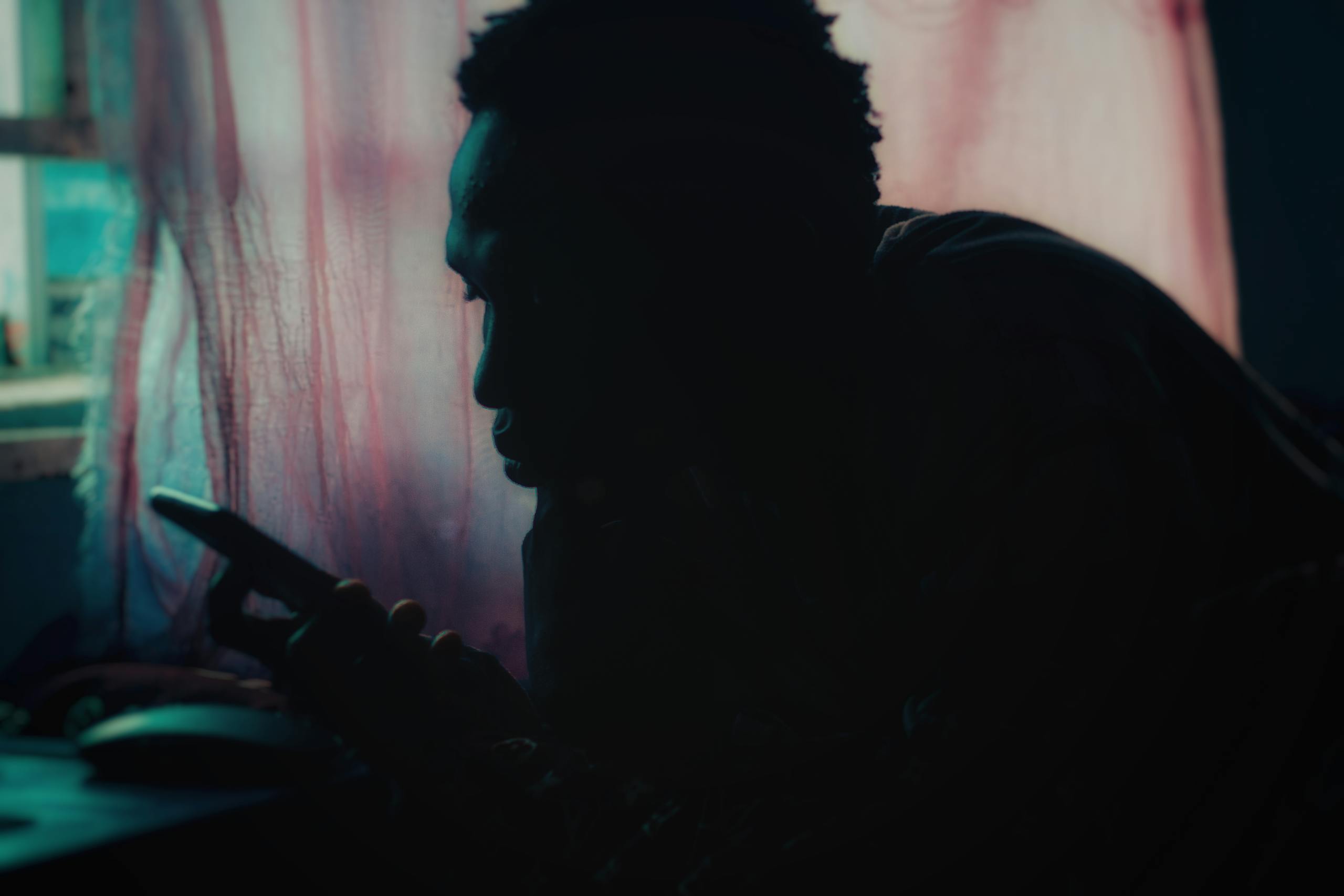 Silhouette of an adult using a smartphone near a window with soft lighting and moody ambiance.