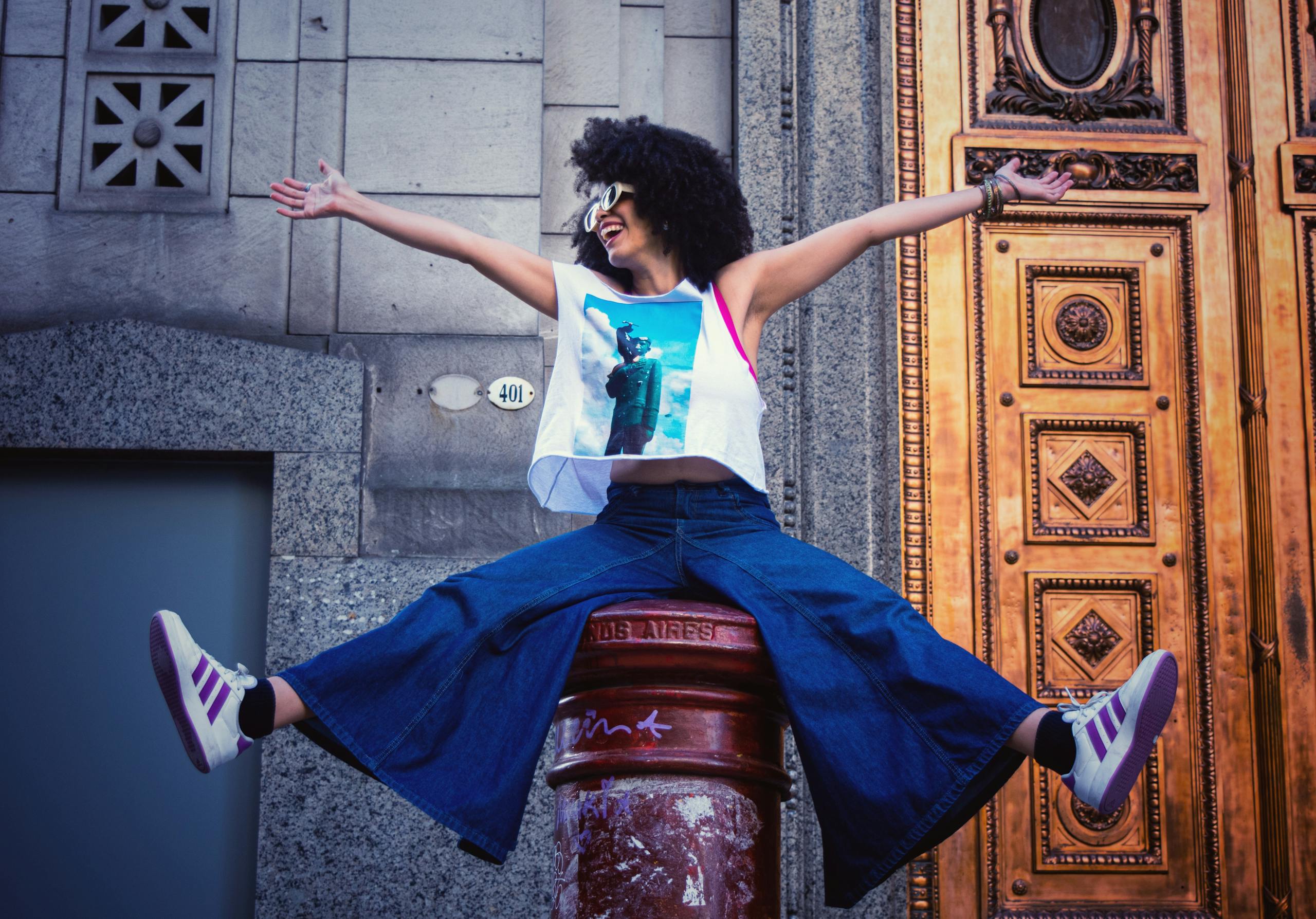 Smiling woman in casual attire poses playfully outdoors against a decorative door.