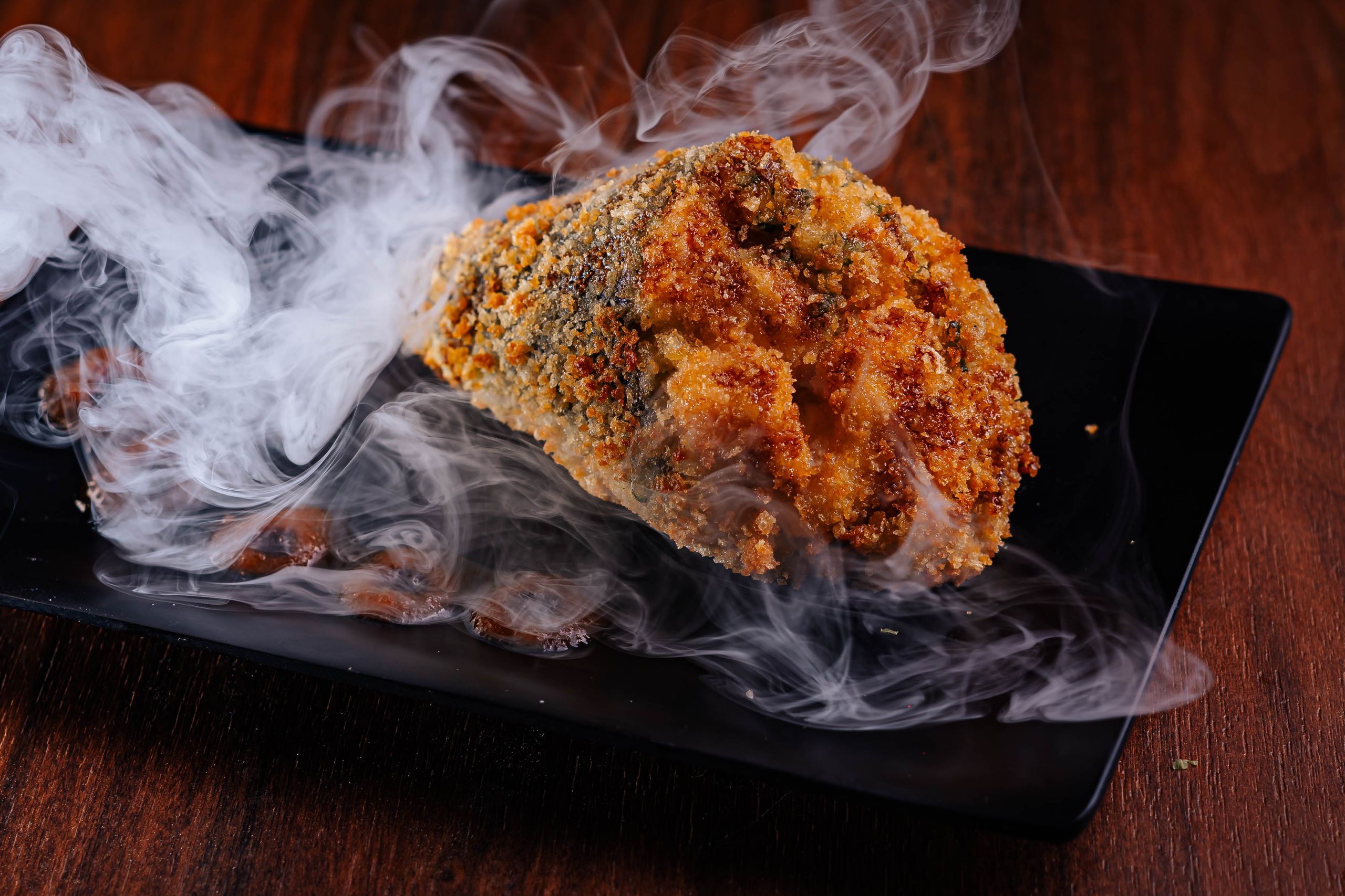 Smoky, crispy fried appetizer served on a black plate for a gourmet presentation.