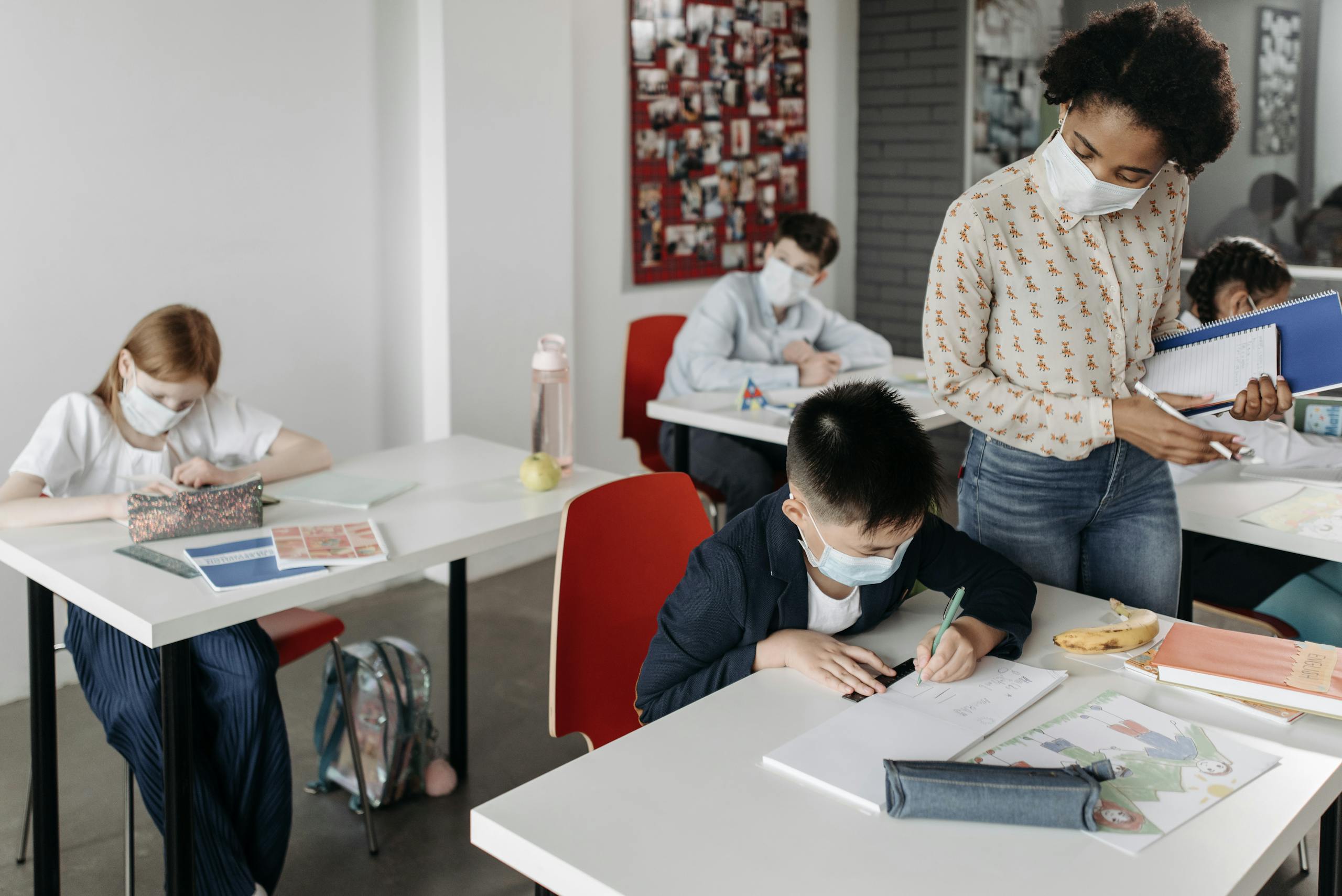 Students and teacher in a classroom setting during pandemic wearing face masks and practicing safety measures.