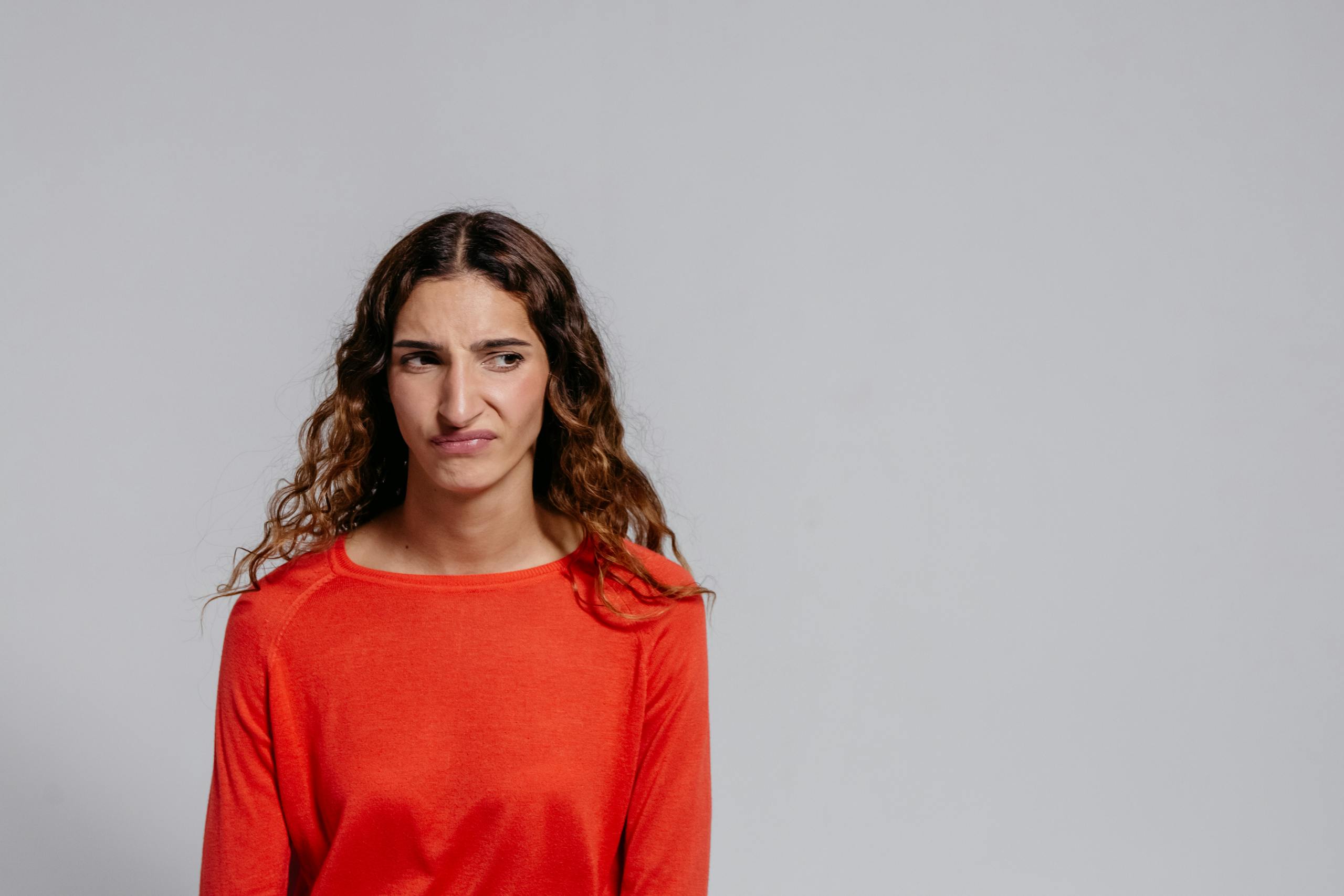 Studio portrait of a young woman with a displeased expression wearing a red sweater.