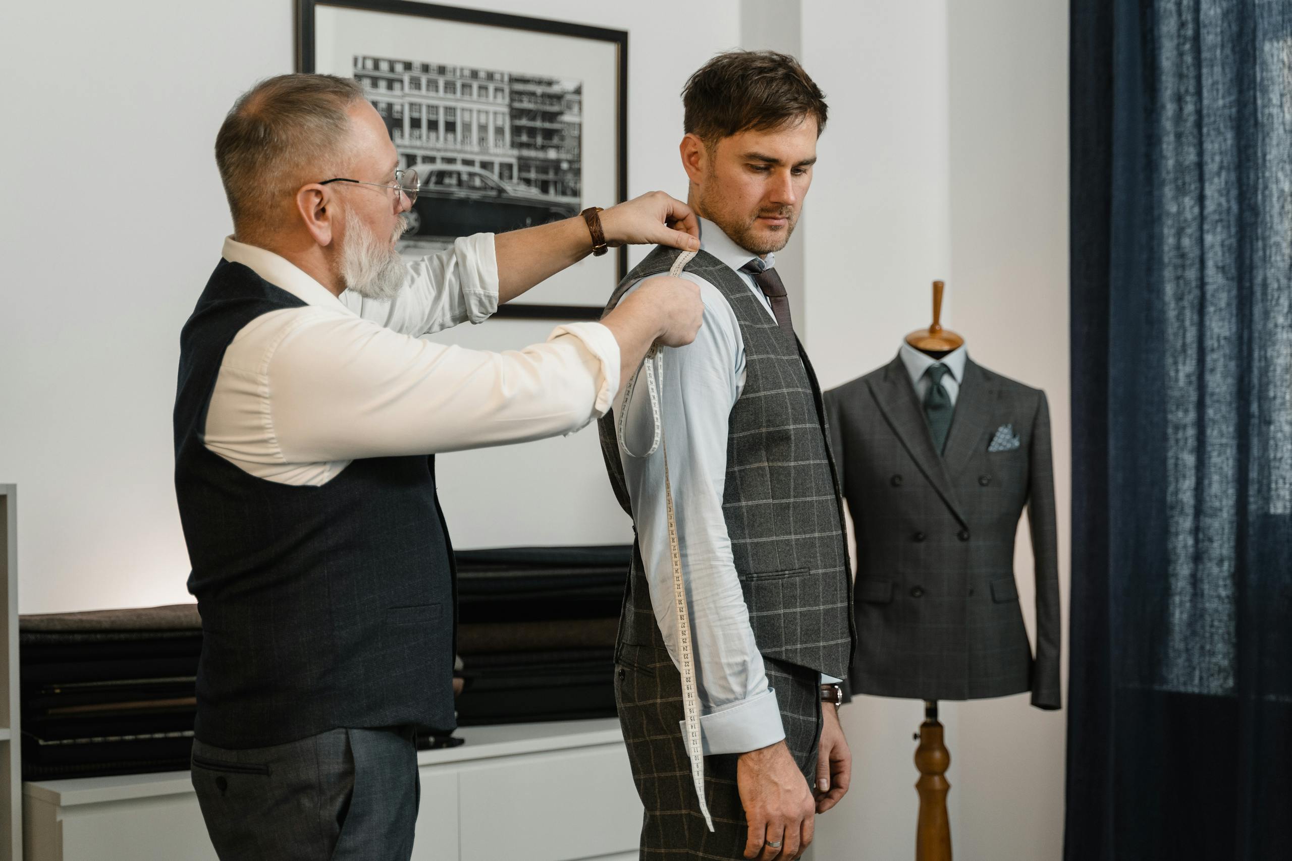 A tailor expertly measuring client for a custom-made suit in a stylish workshop.
