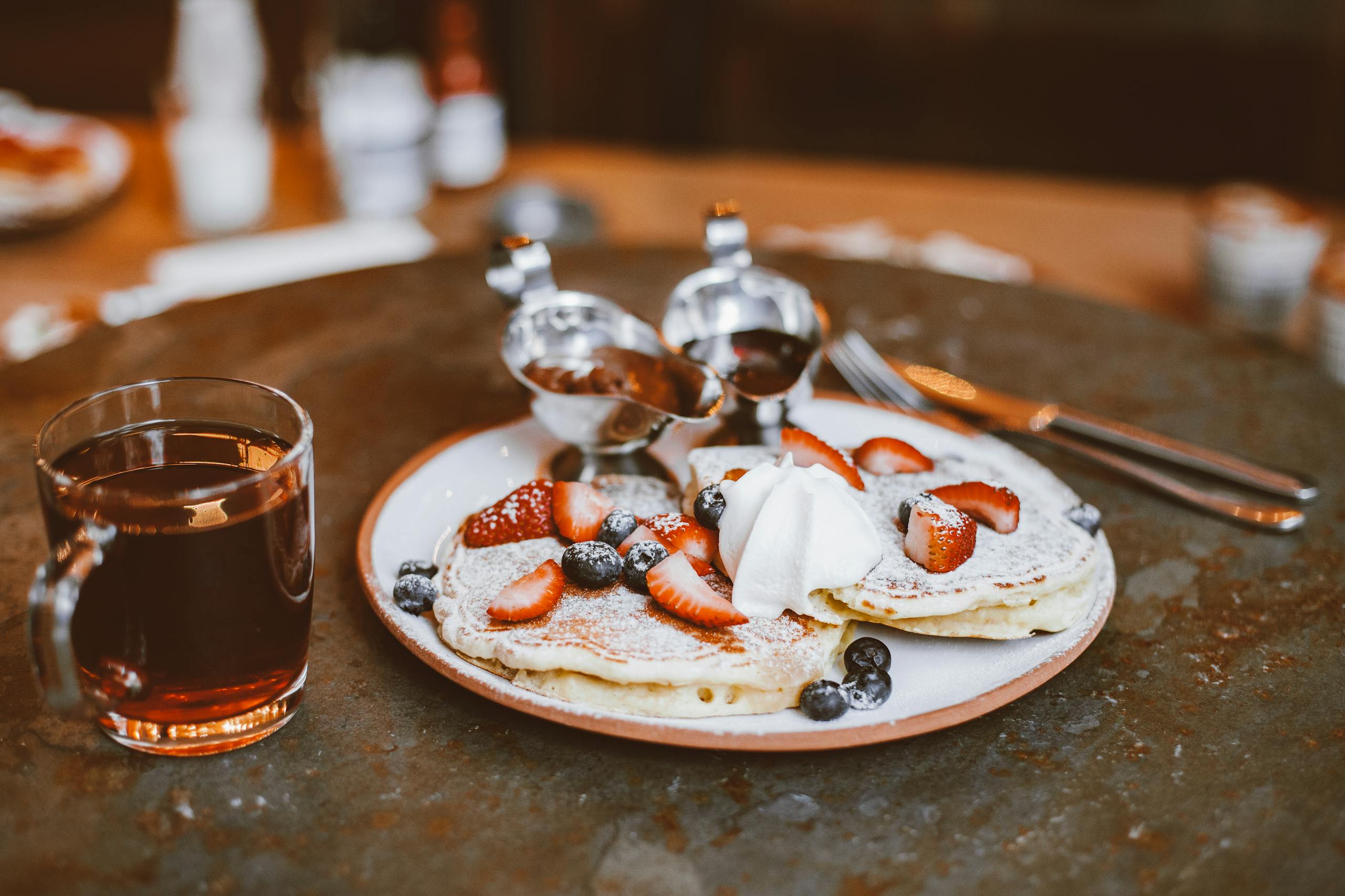 Tasty pancakes topped with strawberries, blueberries, and whipped cream, served with tea.