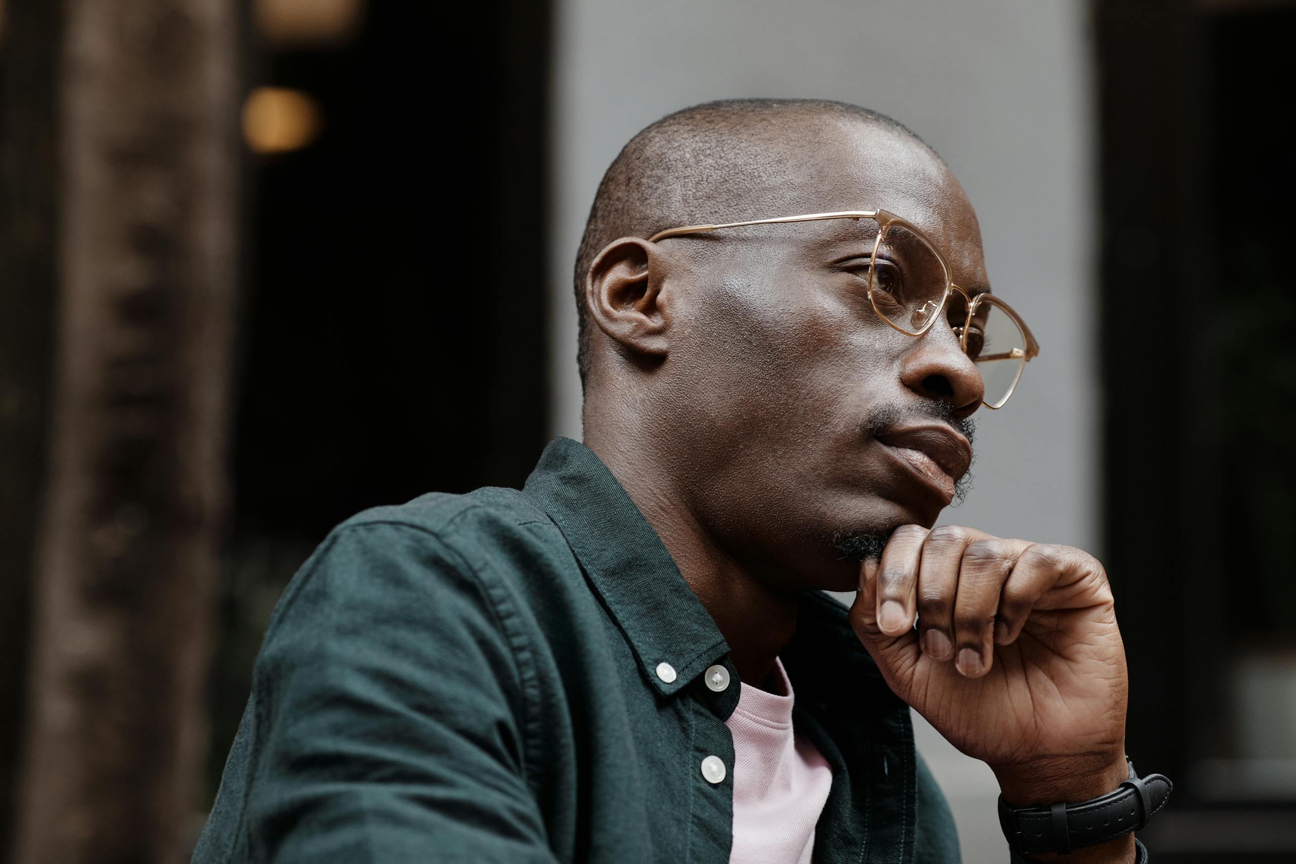 Thoughtful man with glasses sitting outdoors in contemplation.