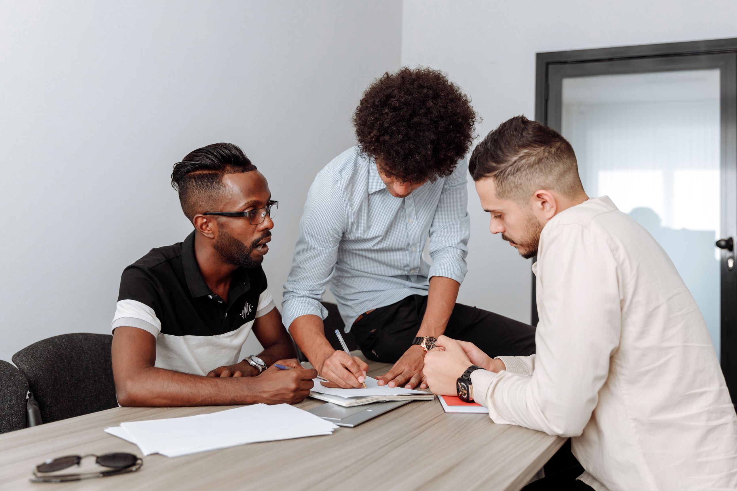 Three diverse men engaged in a business meeting, planning and writing in an office.
