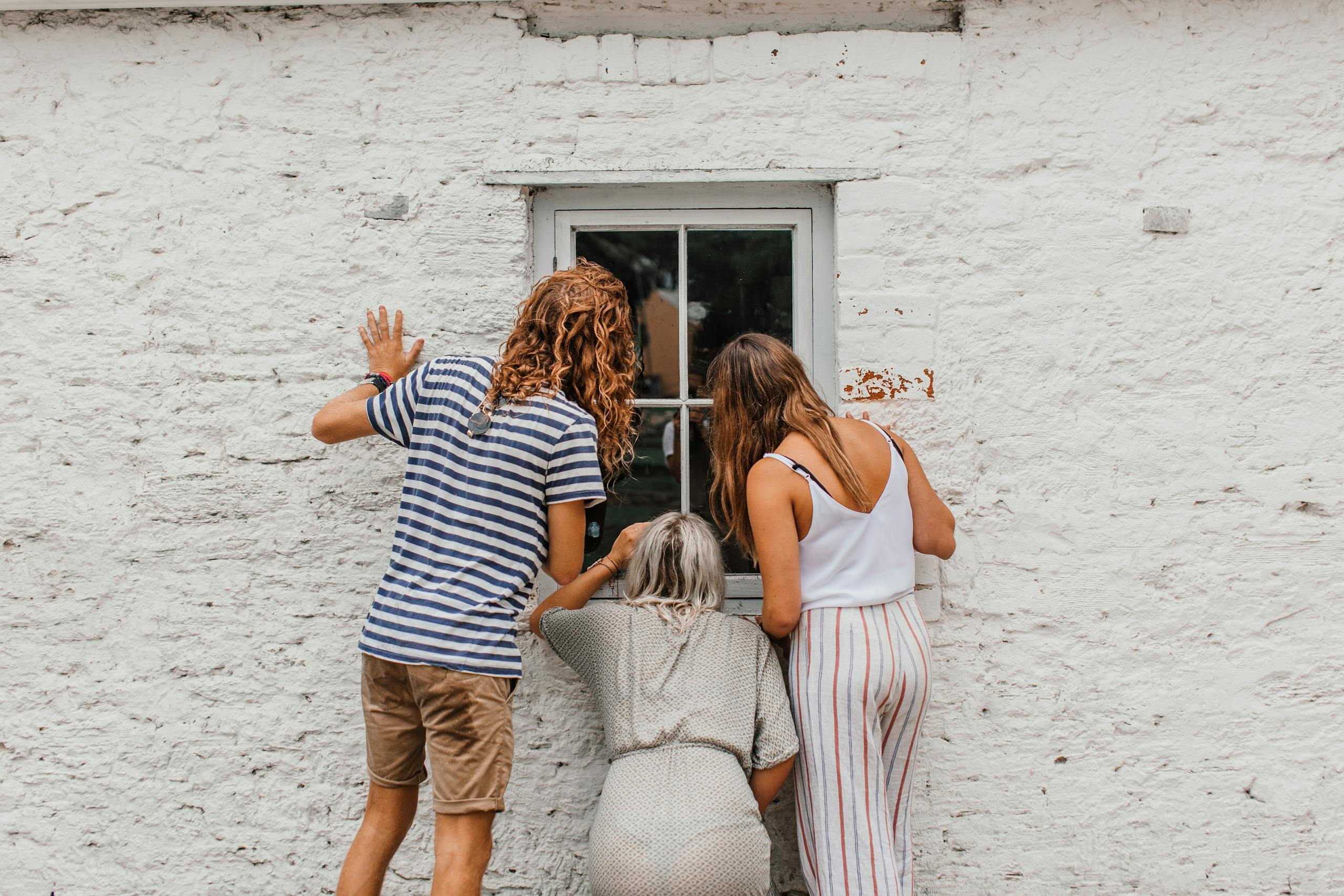 Three people peering through a window in a white wall. Captures curiosity and exploration.