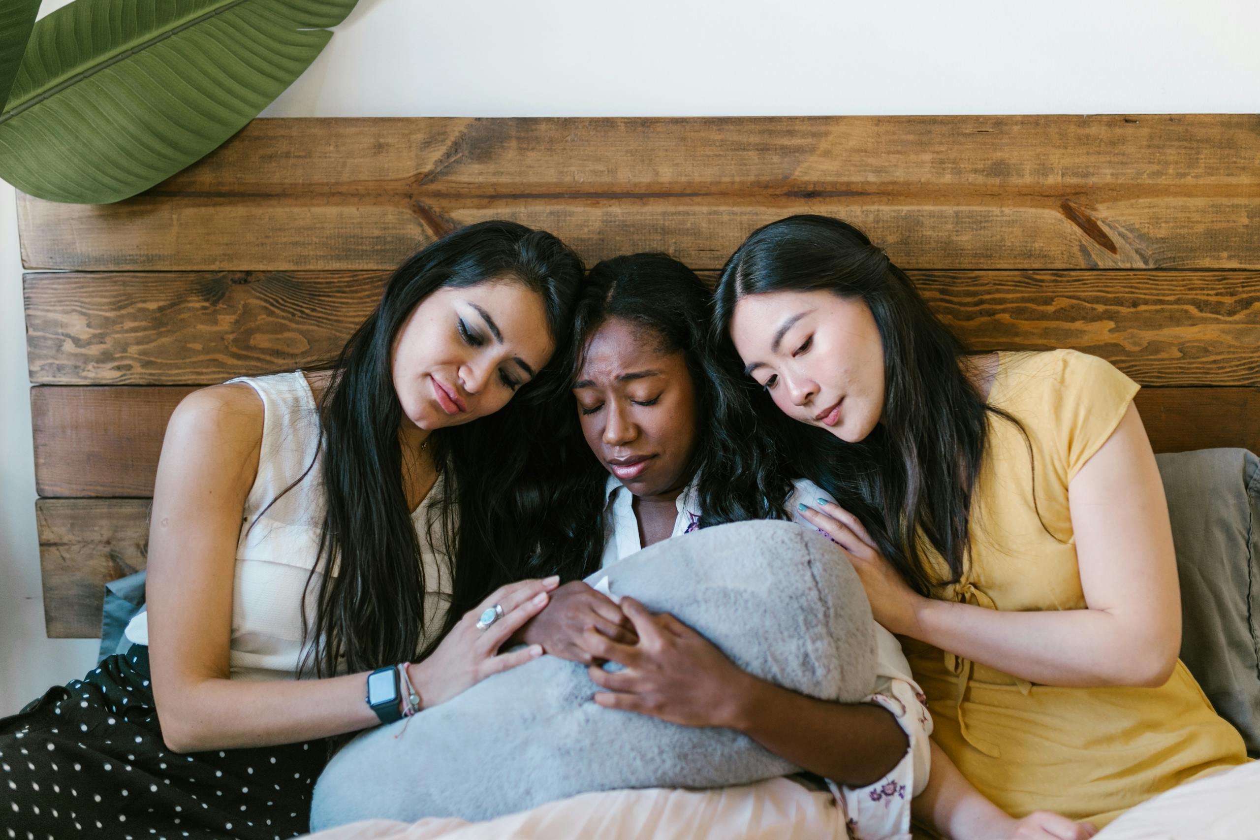 Three women showing support and comfort to a friend indoors on a bed.