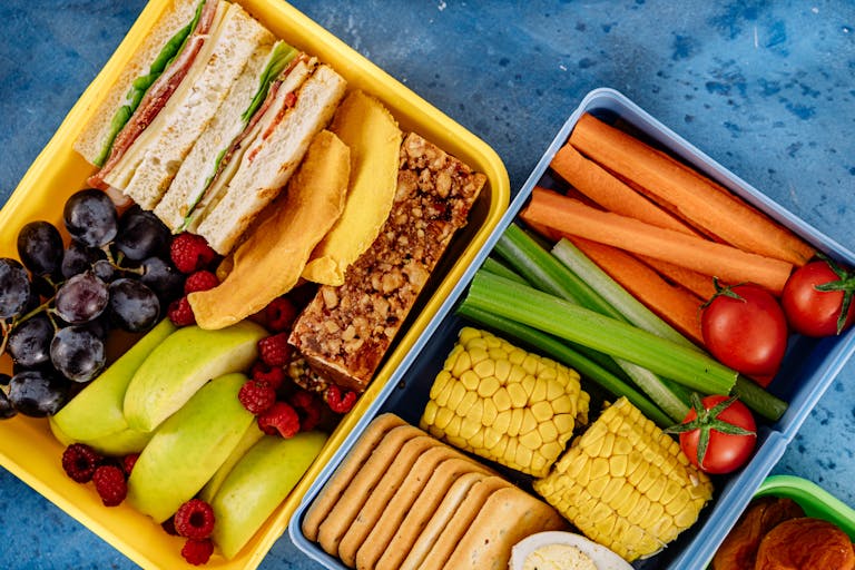Top view of a nutritious packed lunchbox with sandwiches, vegetables, and fruits.