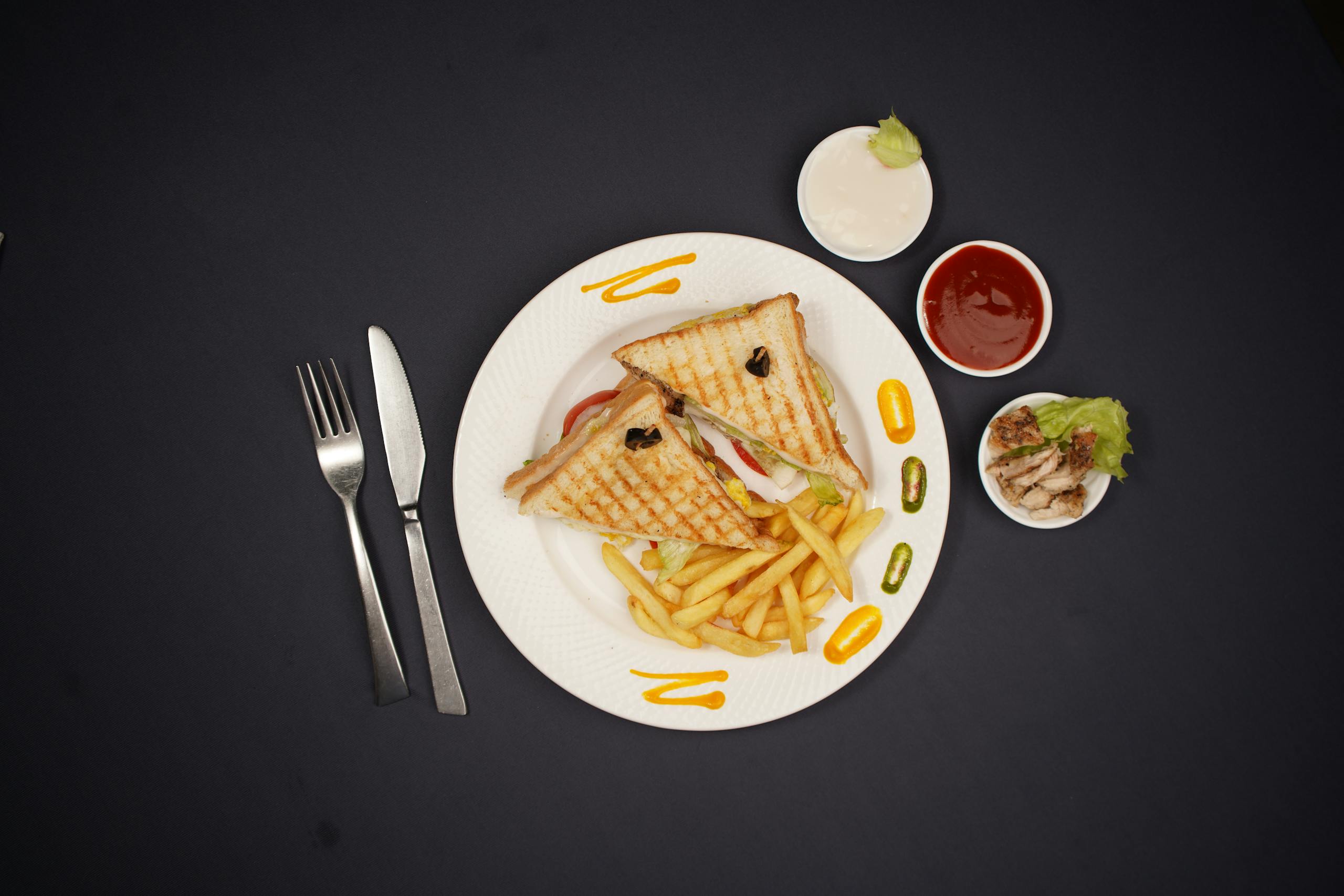 Top view of a sandwich with fries, mayonnaise, ketchup, and sauce on a black background.