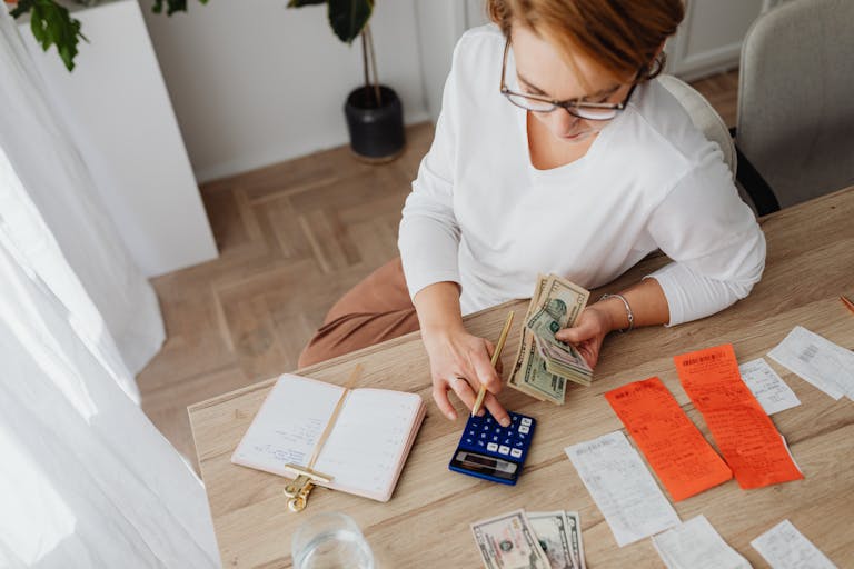 Top view of a woman managing finances with a calculator, cash, and bills in a home setting.