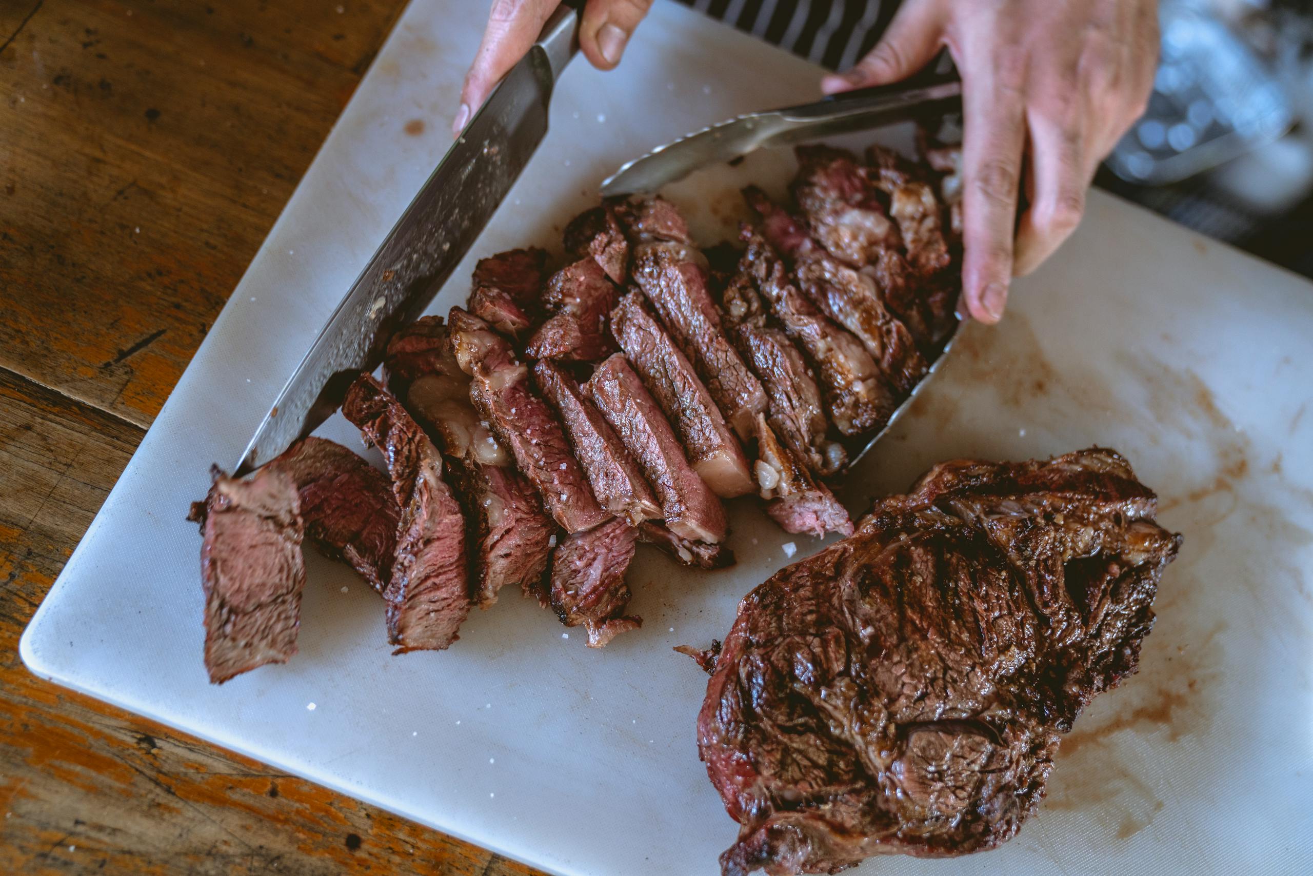 Top view of hands slicing a perfectly grilled steak on a chopping board, showcasing mouthwatering tenderness.