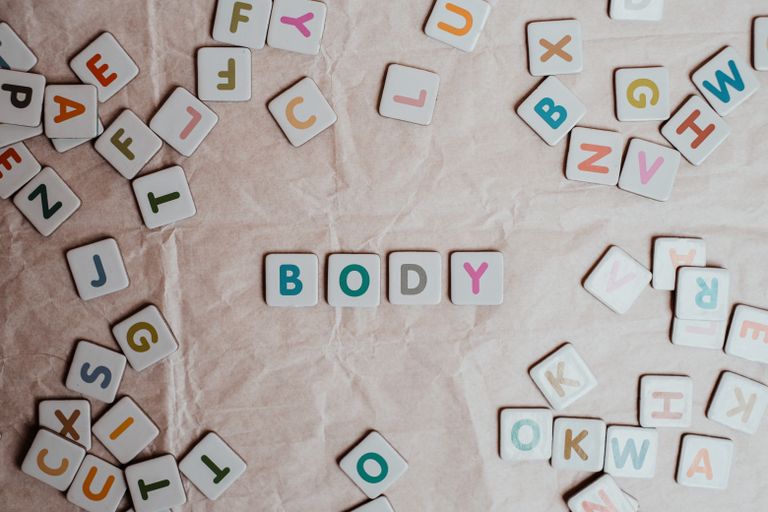 Top view of scattered letter blocks spelling the word 'body' on textured paper.