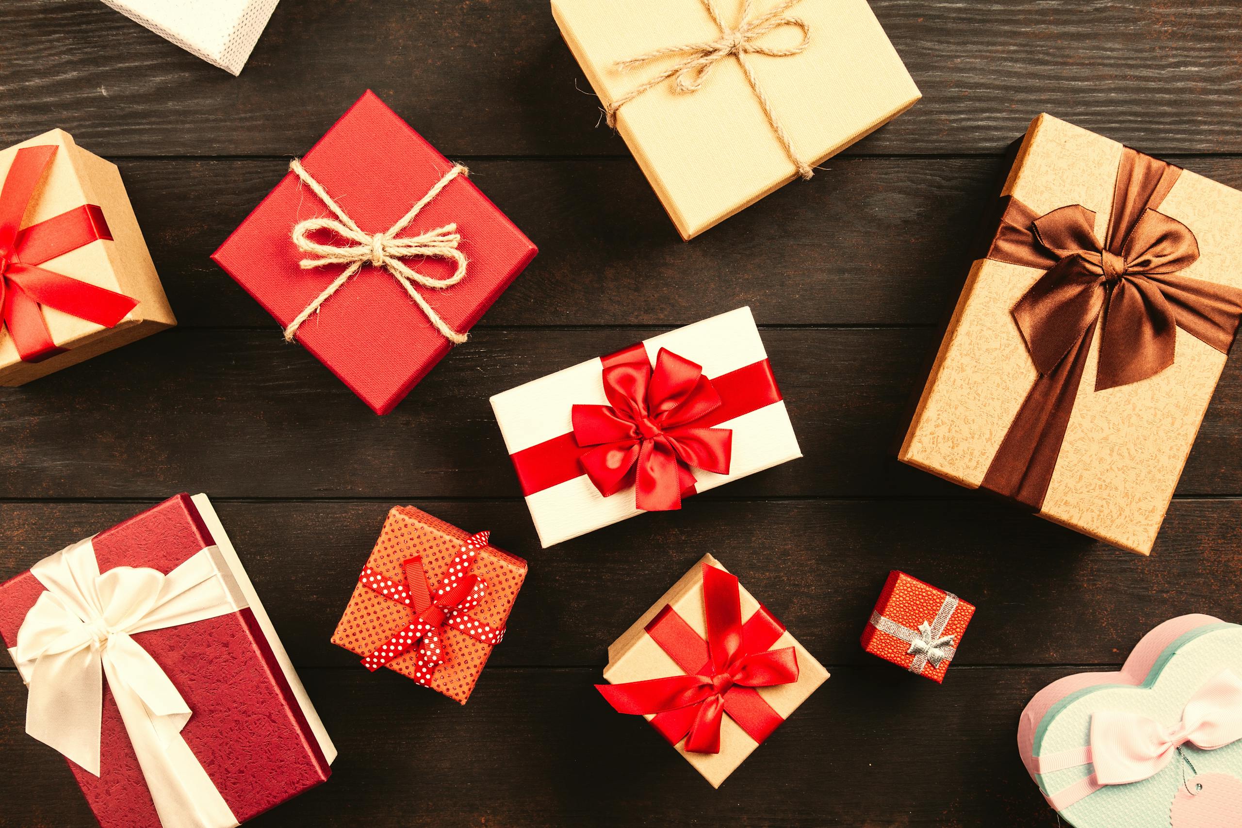 Top view of various wrapped gifts with bows on a wooden table, perfect for Christmas or celebrations.