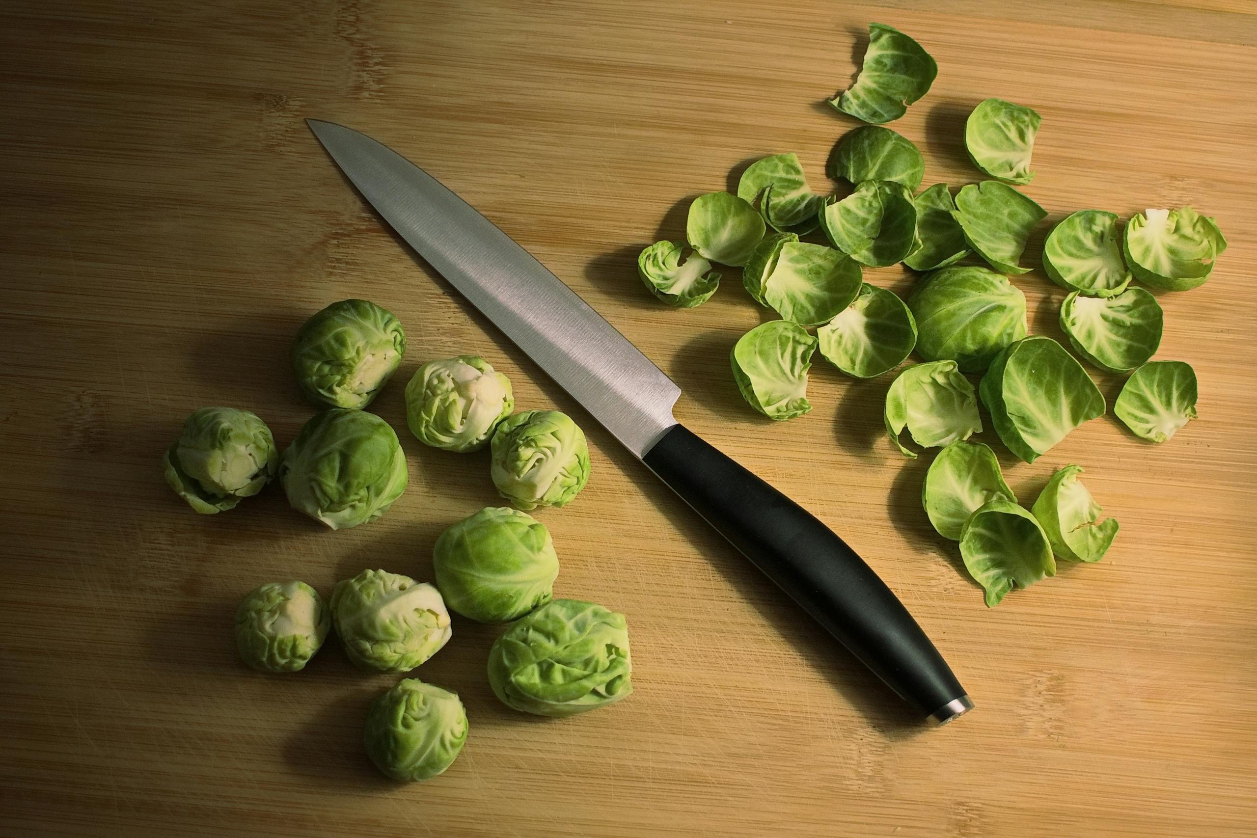 Top view of wooden surface with knife after peeling green fresh Brussels sprouts in kitchen