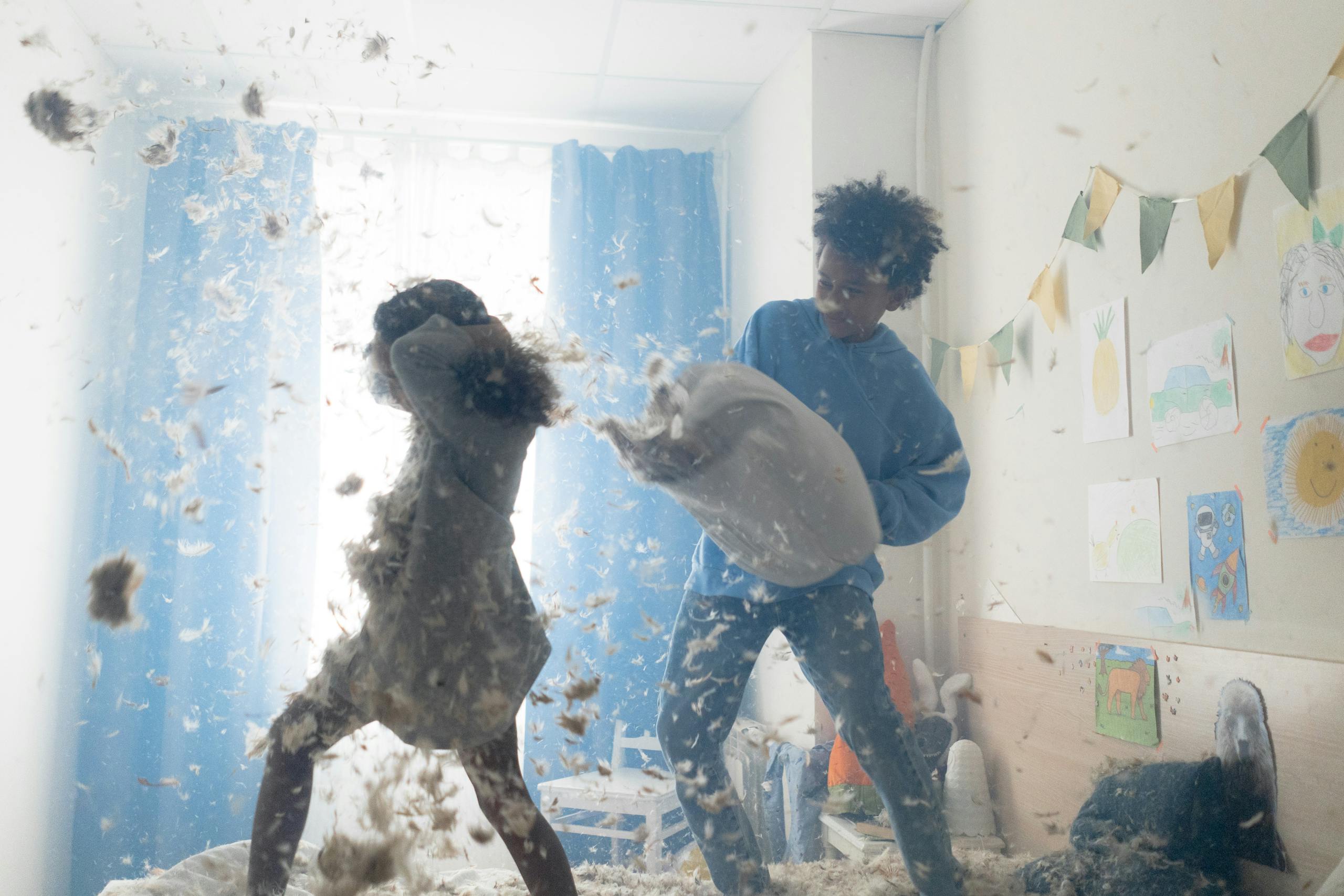 Two children having a playful pillow fight, feathers flying around a vibrant bedroom.