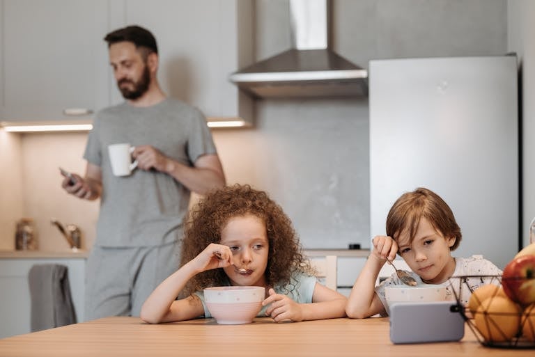 Two children having breakfast while a parent enjoys coffee in a modern kitchen.