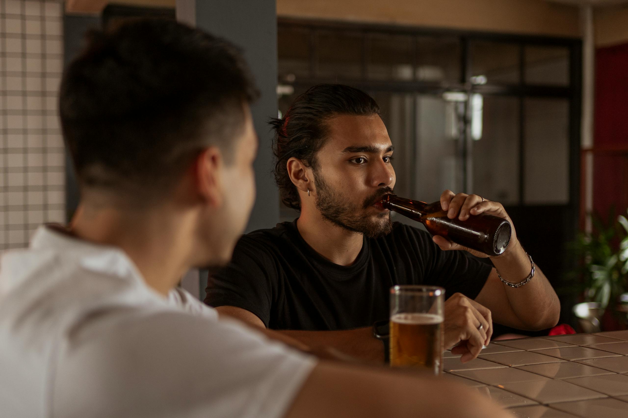 Two men enjoying drinks at a cozy indoor bar setting, capturing a relaxed social vibe.