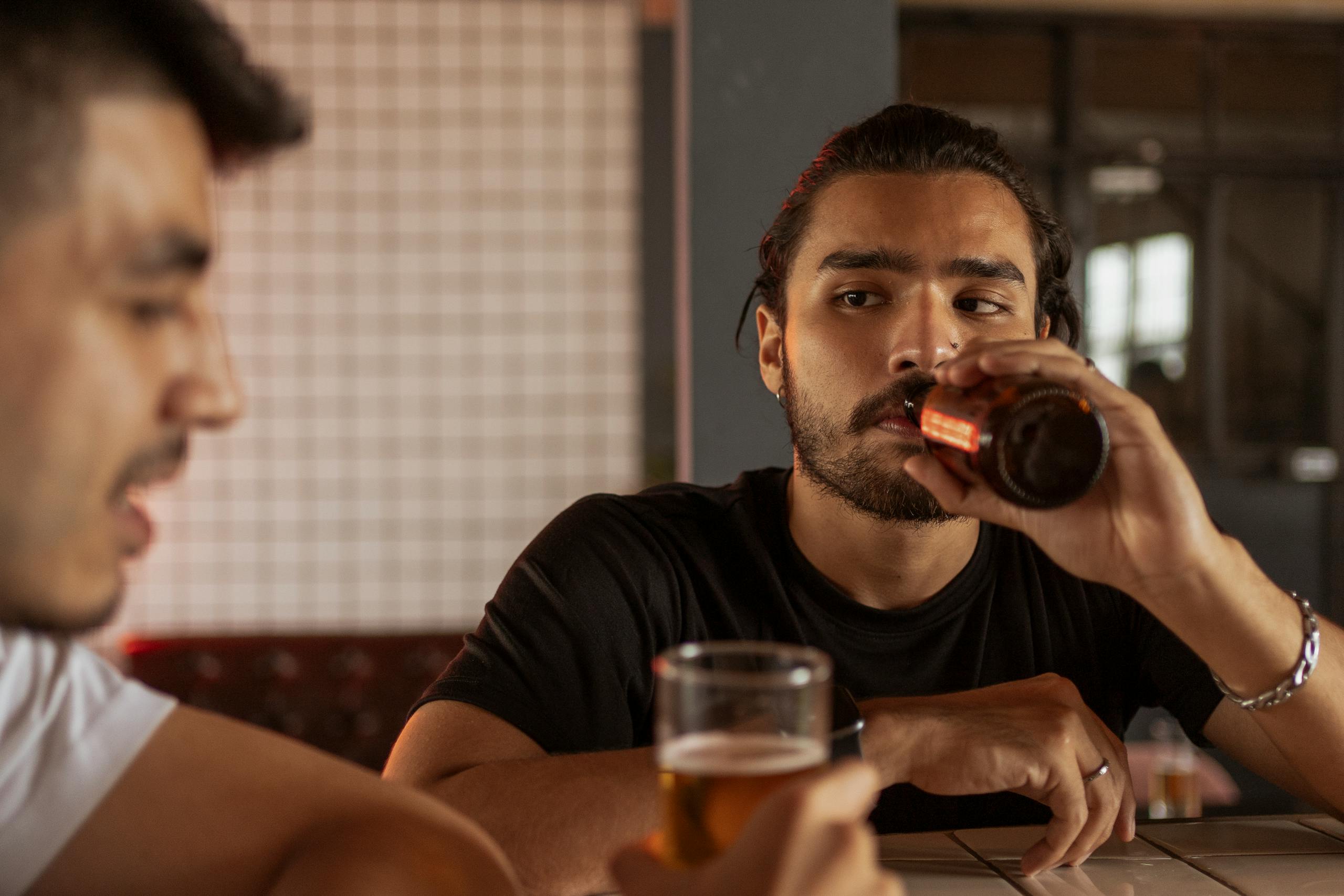 Two men having a conversation while enjoying beers at a bar, creating a social and relaxed atmosphere.