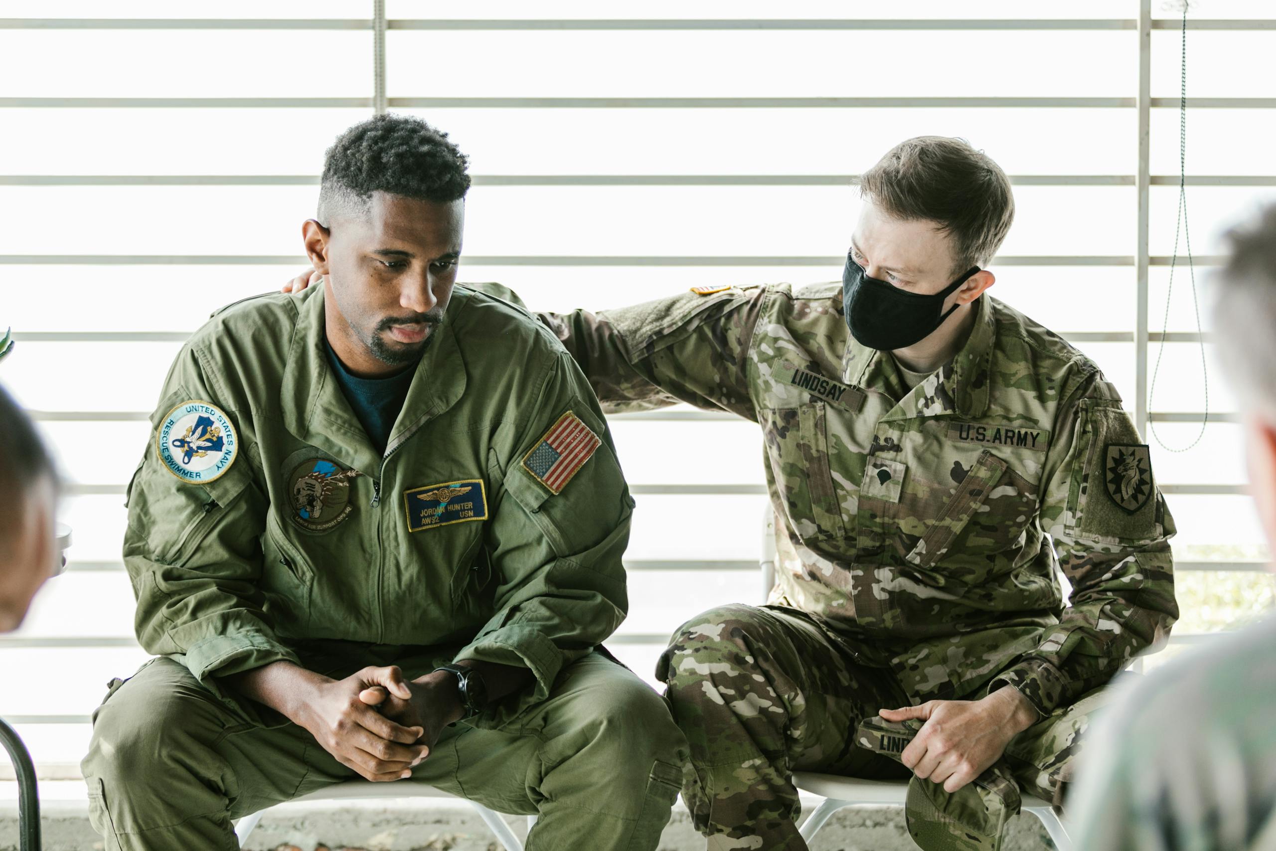 Two military personnel engaged in an emotional support session indoors.