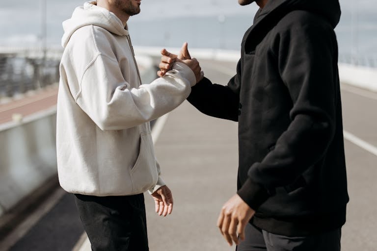 Two people in hoodies shake hands outdoors, symbolizing friendship and connection.