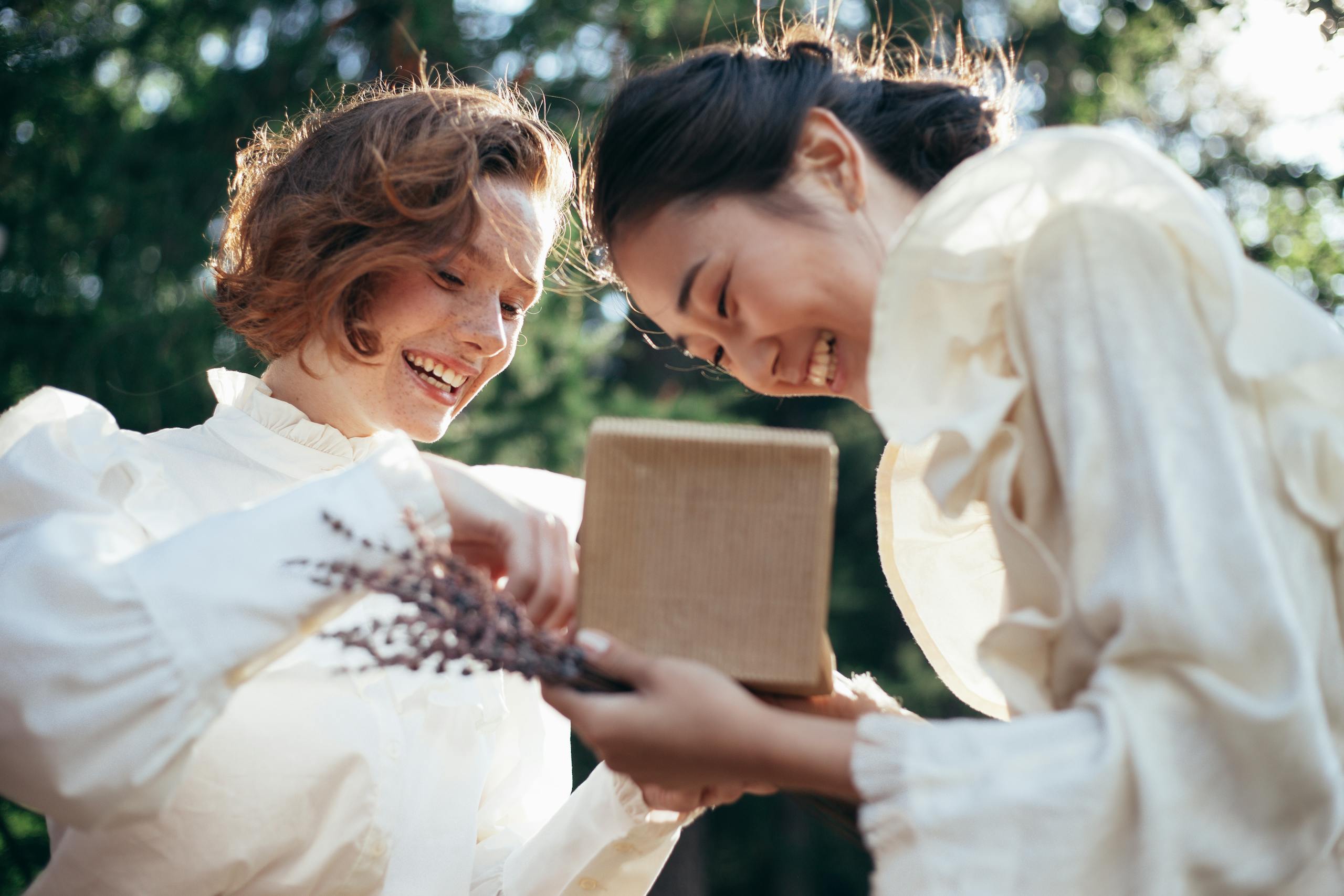 Two women enjoying a heartfelt moment exchanging gifts outdoors, exuding happiness and friendship.