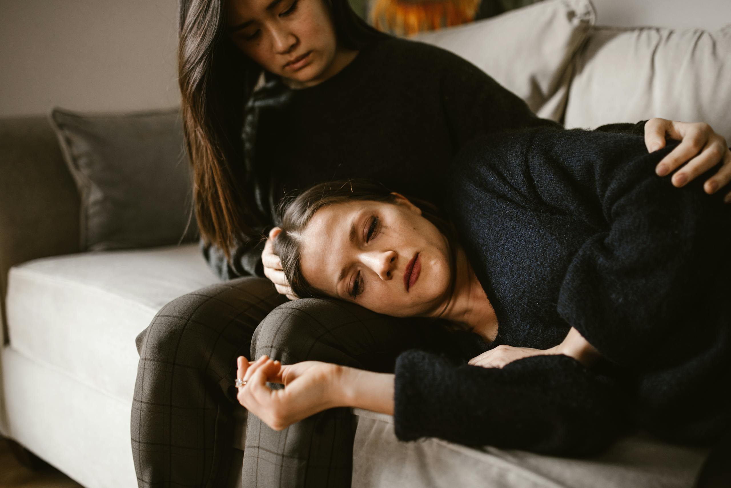 Two women on a couch, one comforting the other, depicting empathy and support.