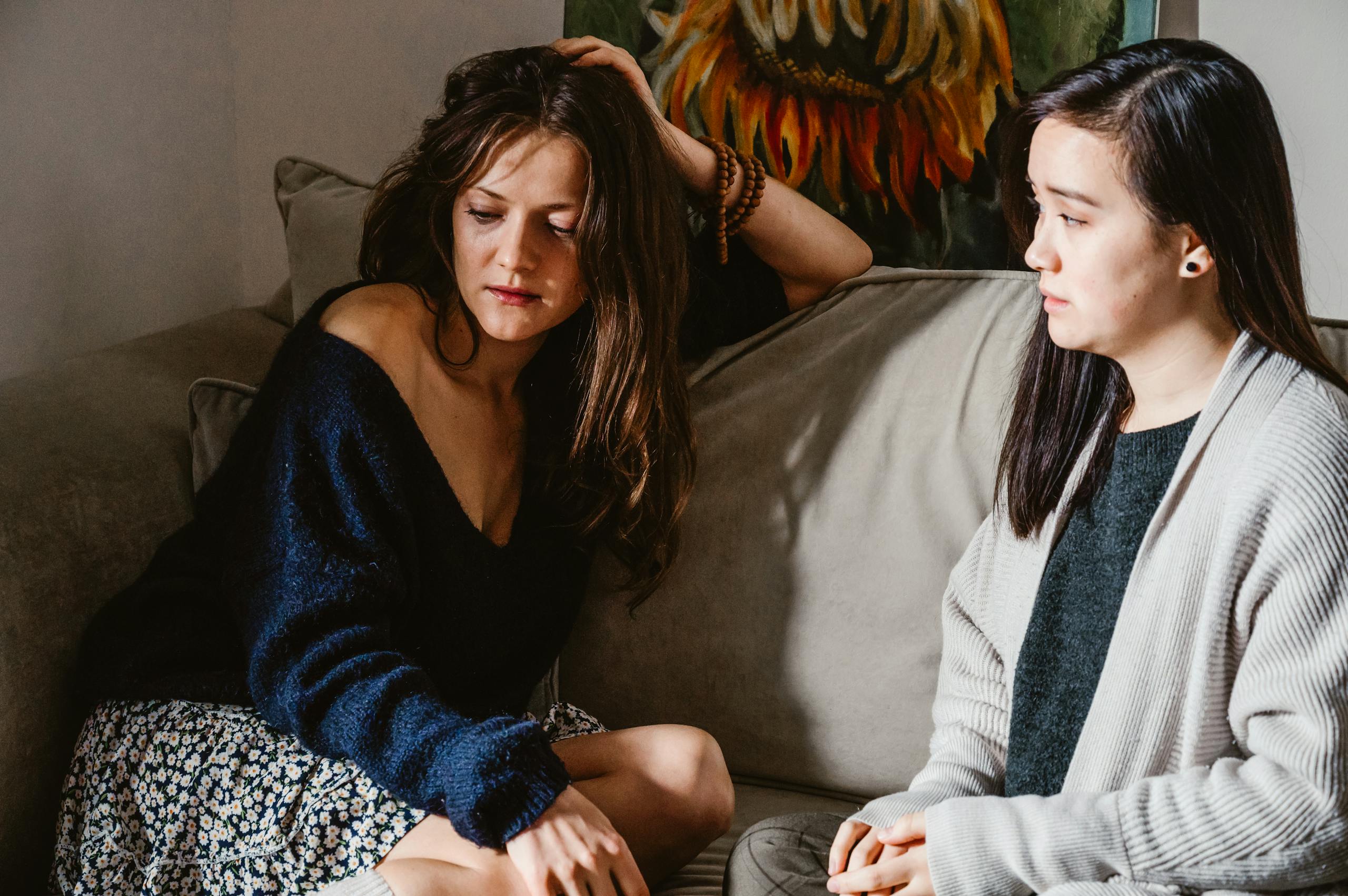 Two women sitting on a sofa engaging in a deep, emotional conversation indoors.