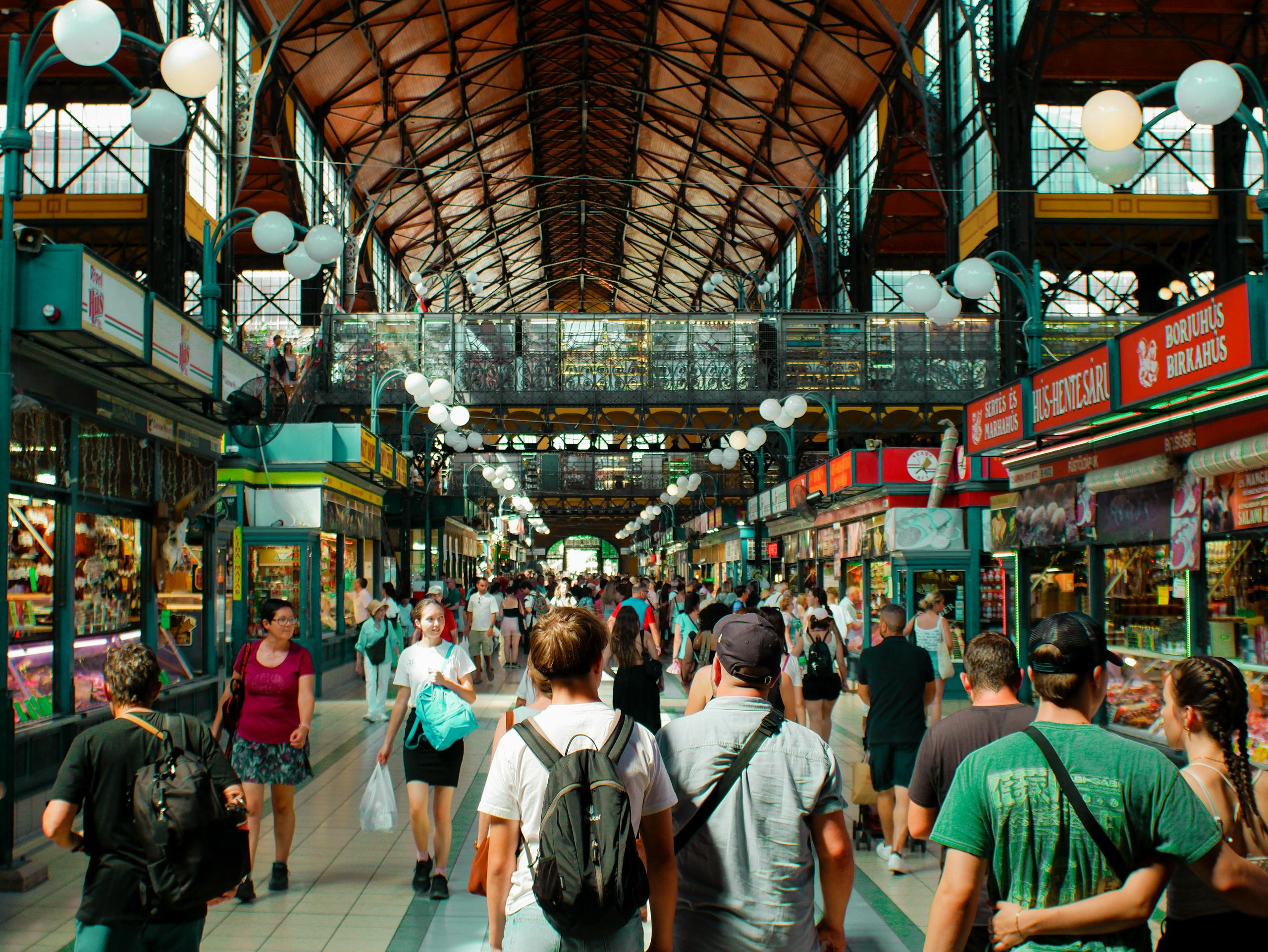 Vibrant indoor market scene with diverse crowd and colorful vendor stalls.