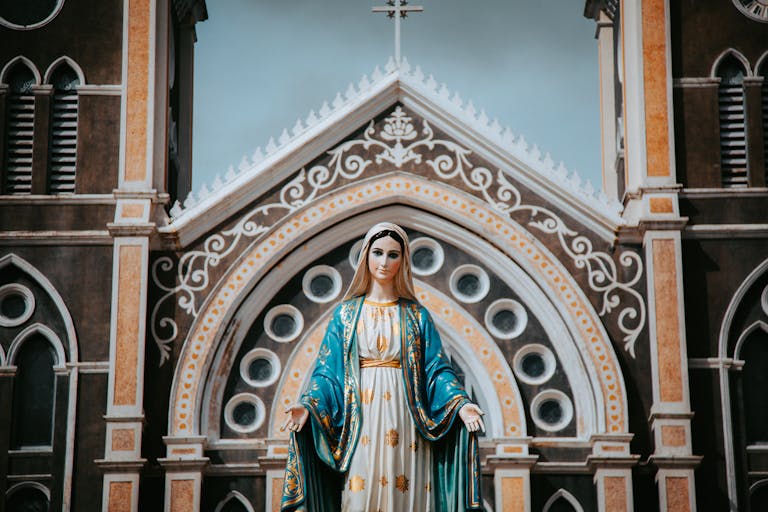 Vibrant statue of the Virgin Mary in front of an ornate church facade.
