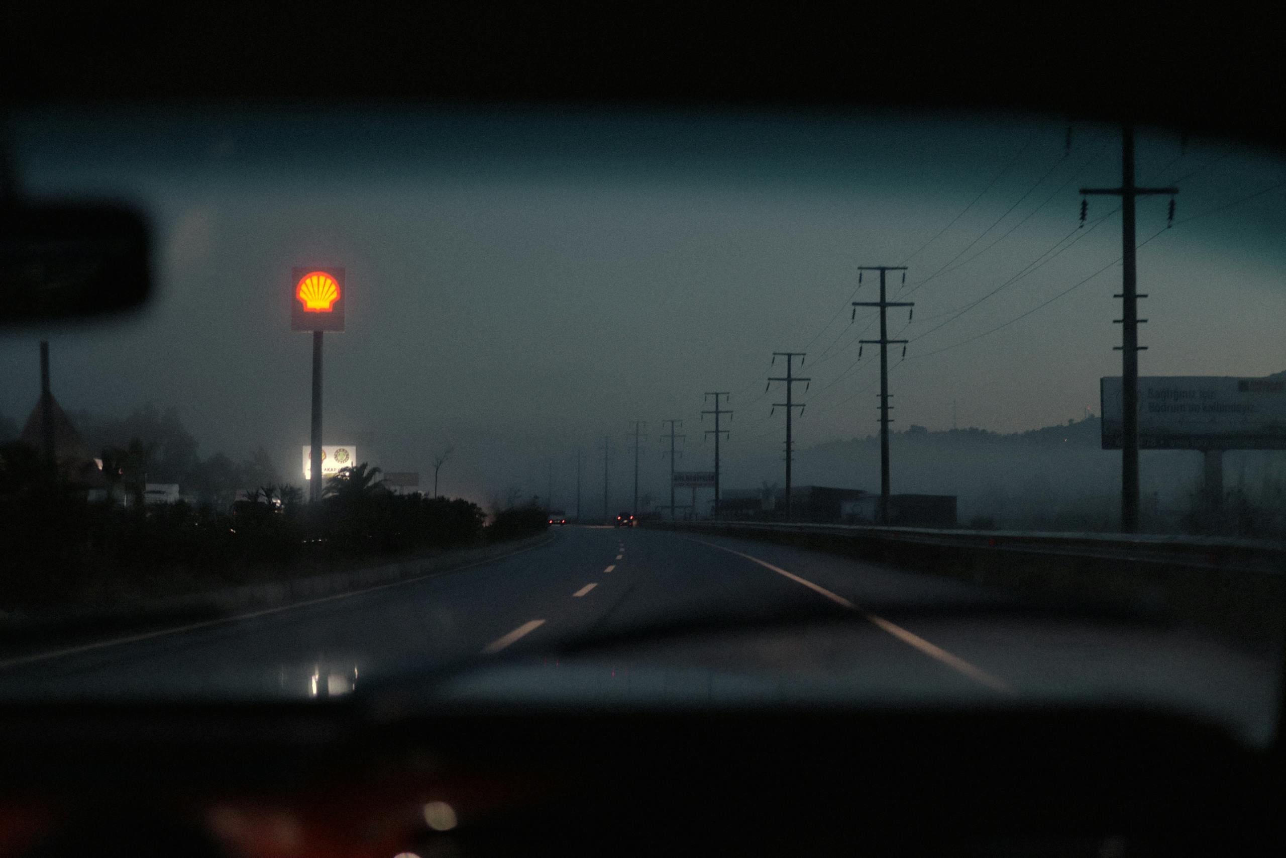 View from a car window of a misty highway at dusk featuring a glowing Shell sign.