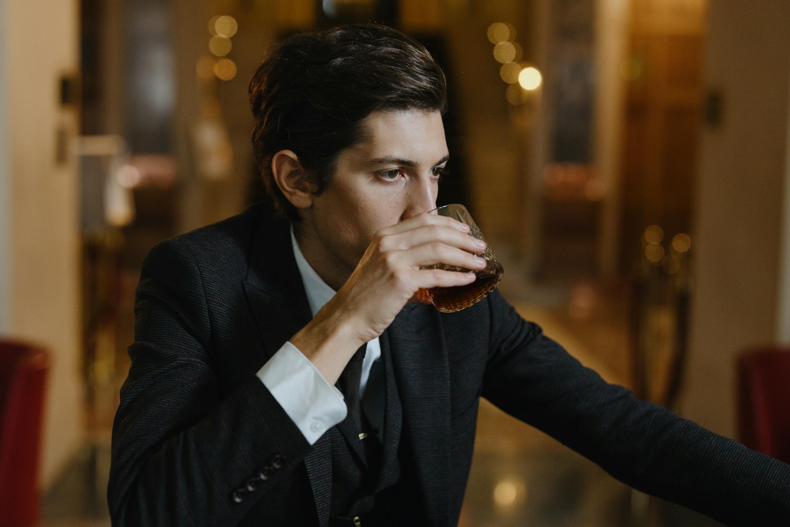 Well-dressed man enjoying a whiskey at a stylish indoor setting. Evening ambiance.