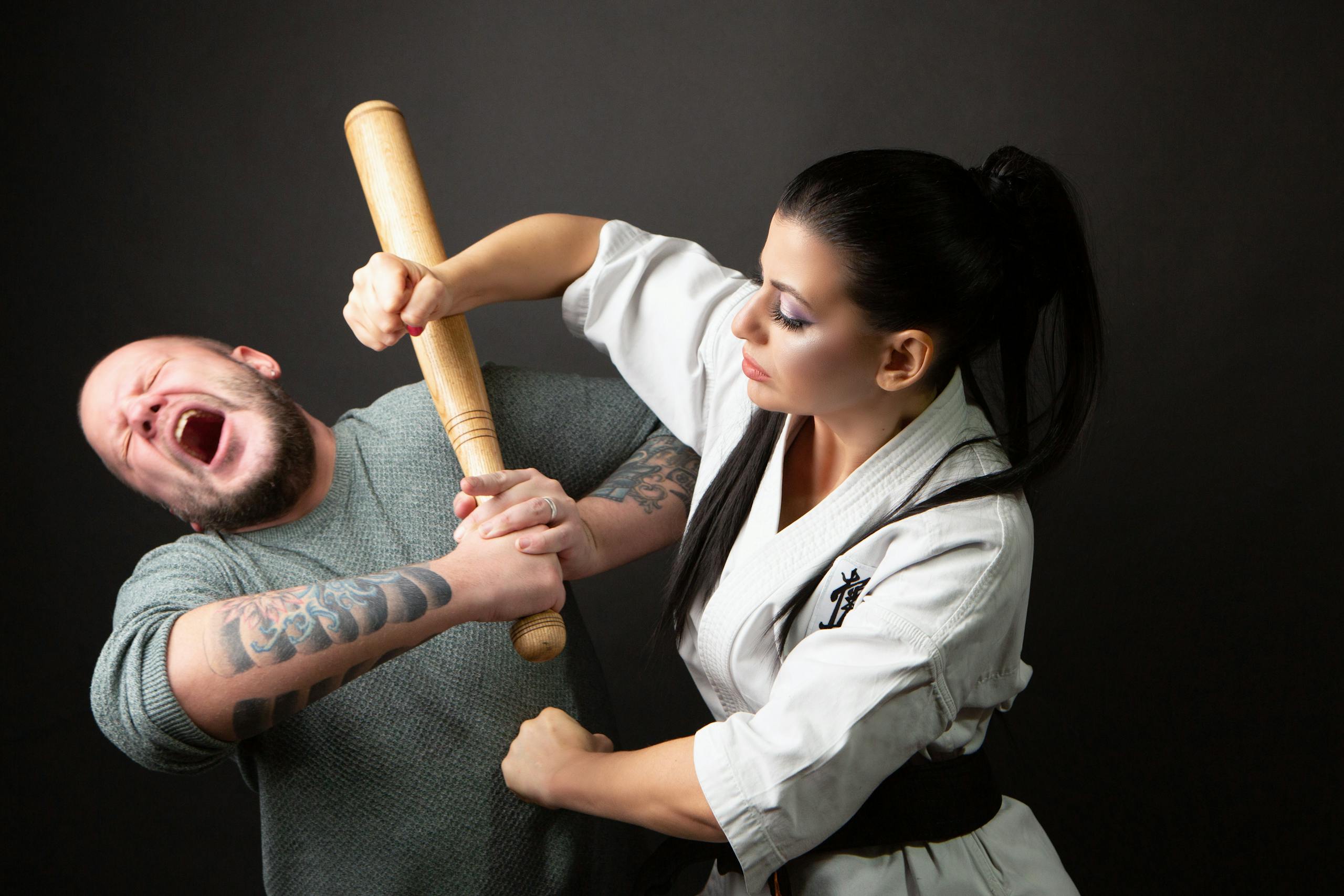 Woman in martial arts training defends against a bearded man's attack with a baton.