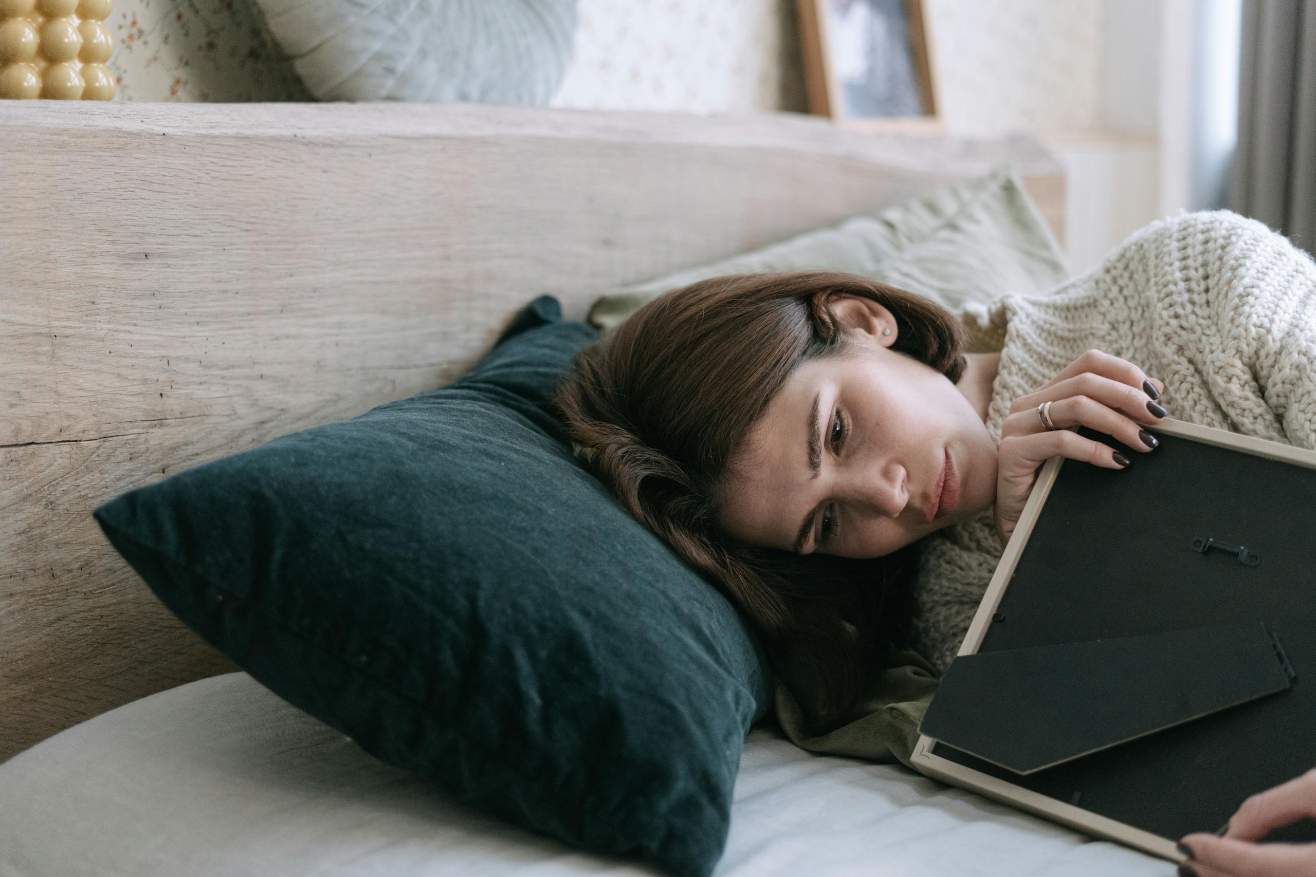 Woman lying in bed holding a picture frame, reflecting quietly indoors.
