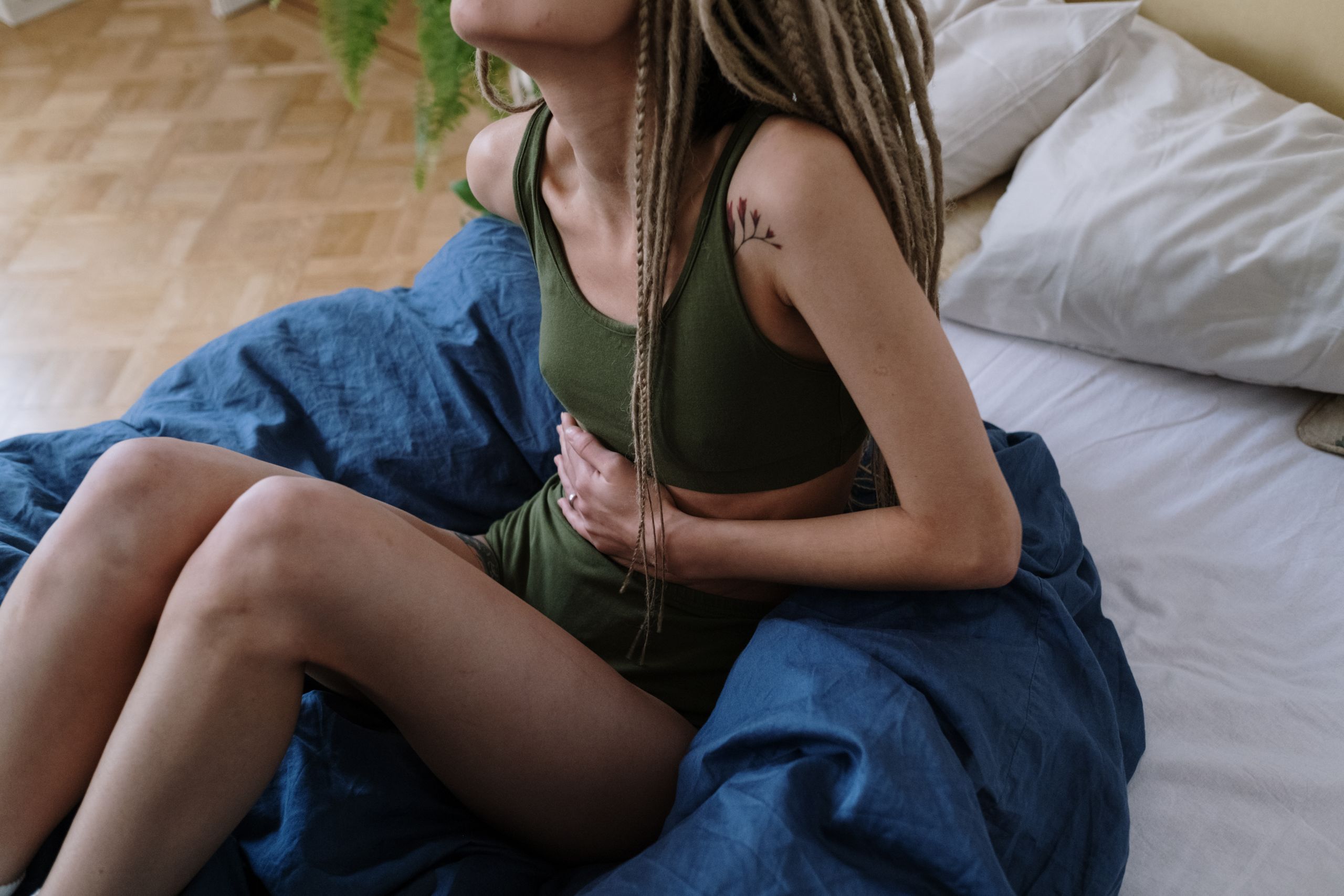 Woman sitting in bed holding her stomach, indicating pain or discomfort, possibly due to cramps.