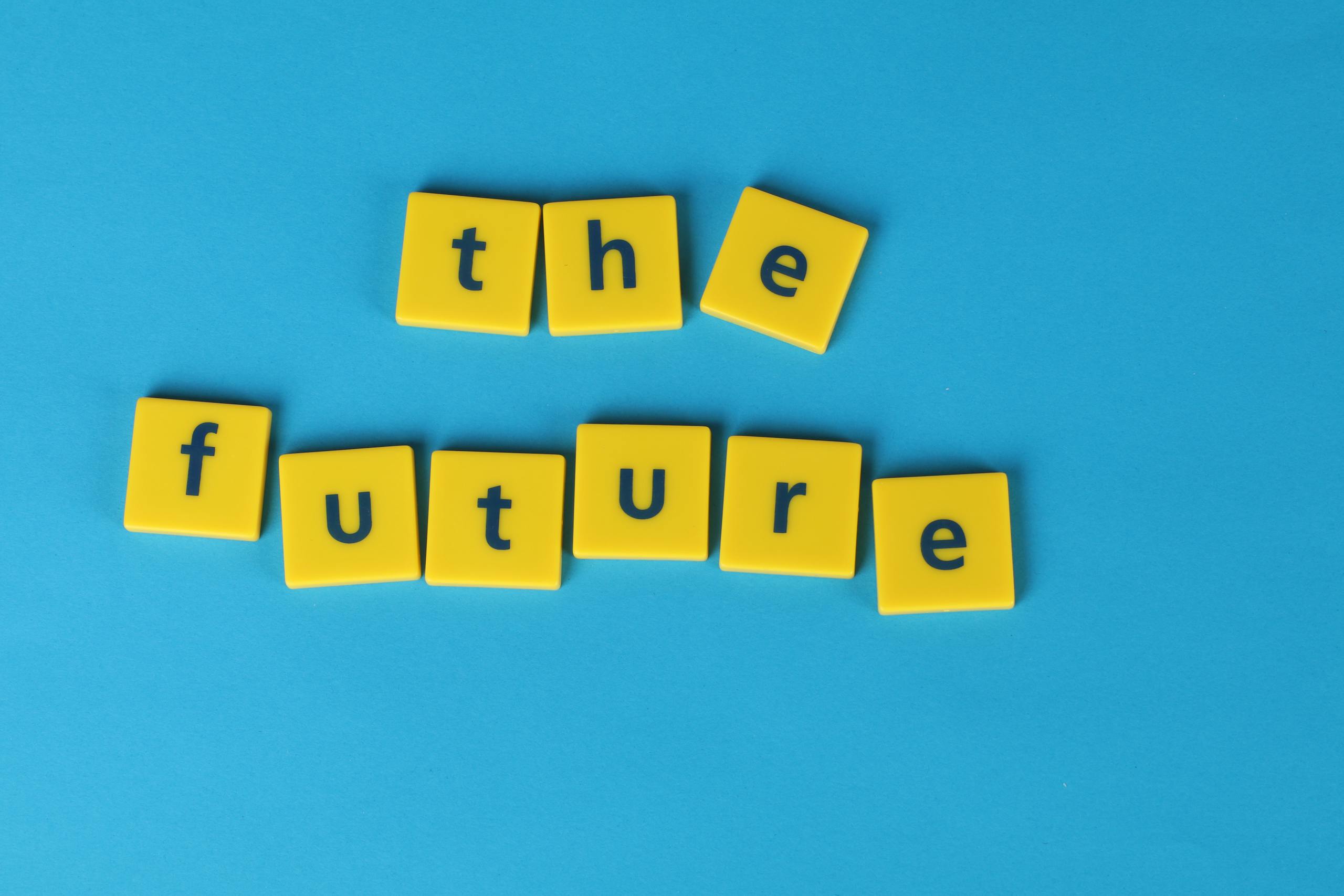 Yellow letter tiles spelling 'the future' on a blue surface, minimalist style.