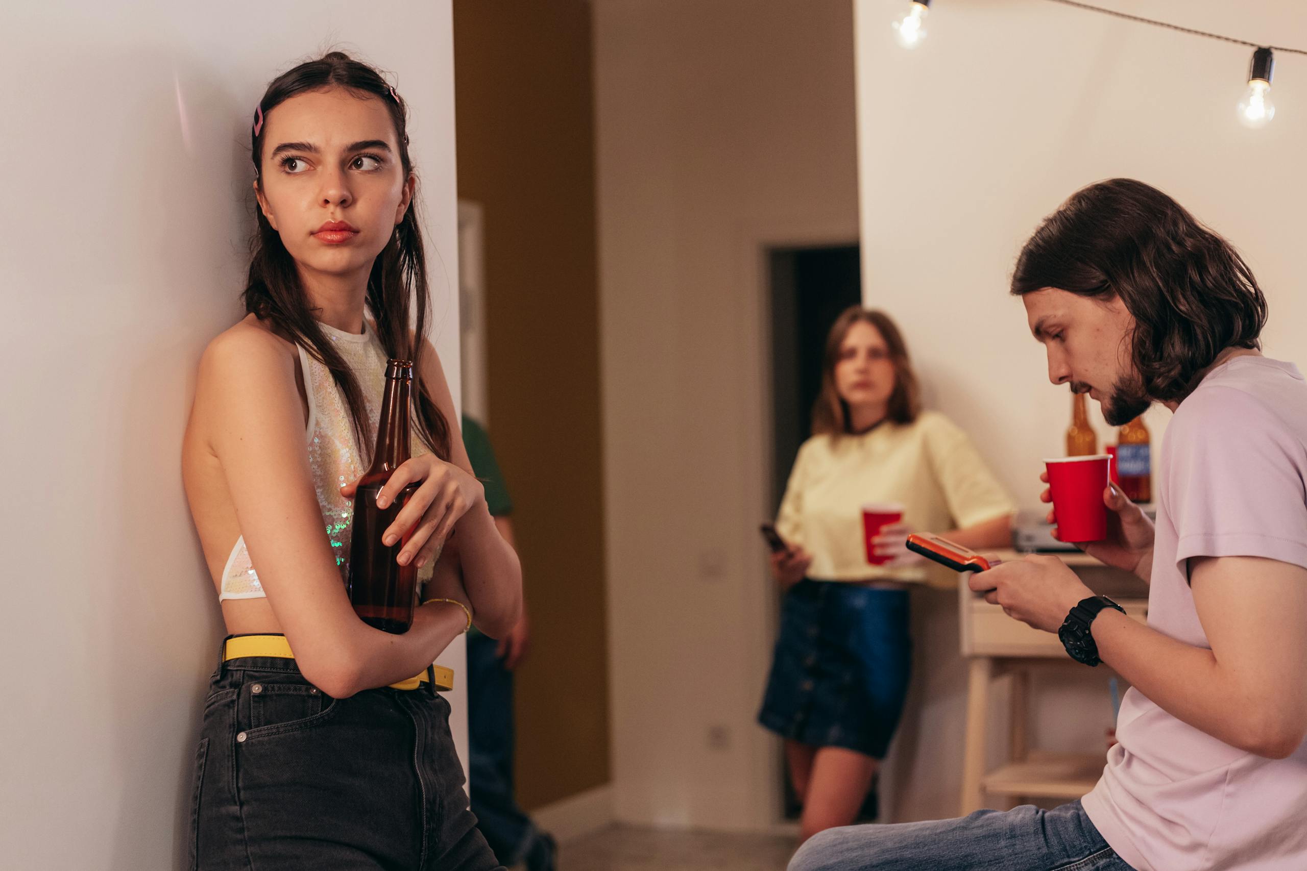 Young adults gather indoors enjoying a casual party with drinks and socializing.