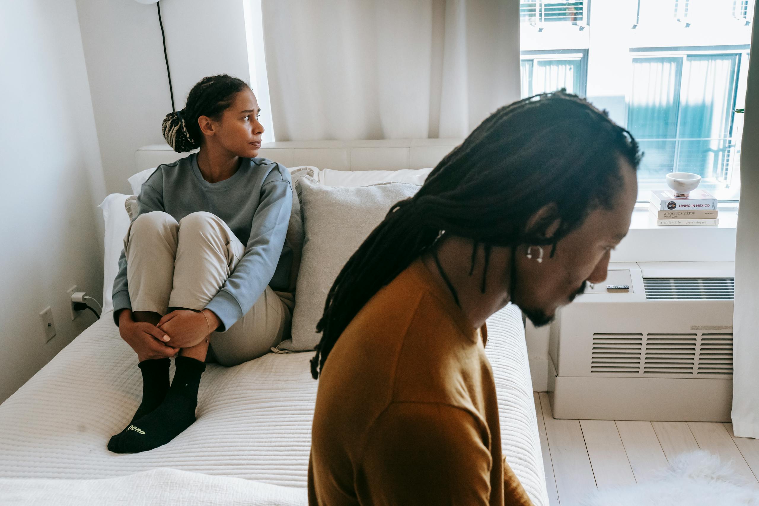Young African American couple in casual clothes resting on bed with sad face in daytime