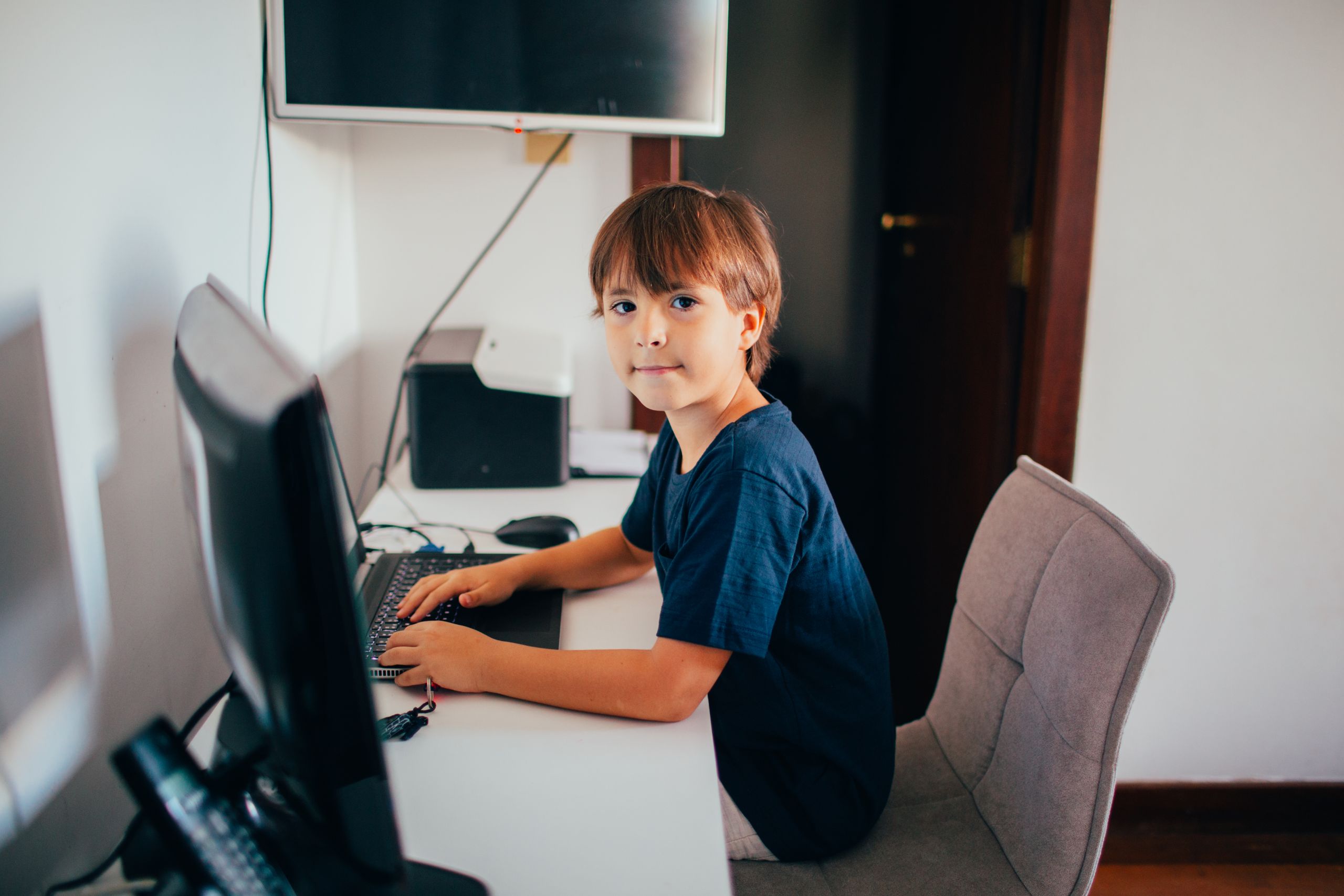 Young boy sitting at a desk using a computer in a home office setting.