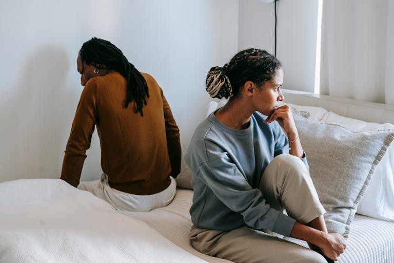 Young discontented African American female touching chin near anonymous male partner during dispute in bedroom