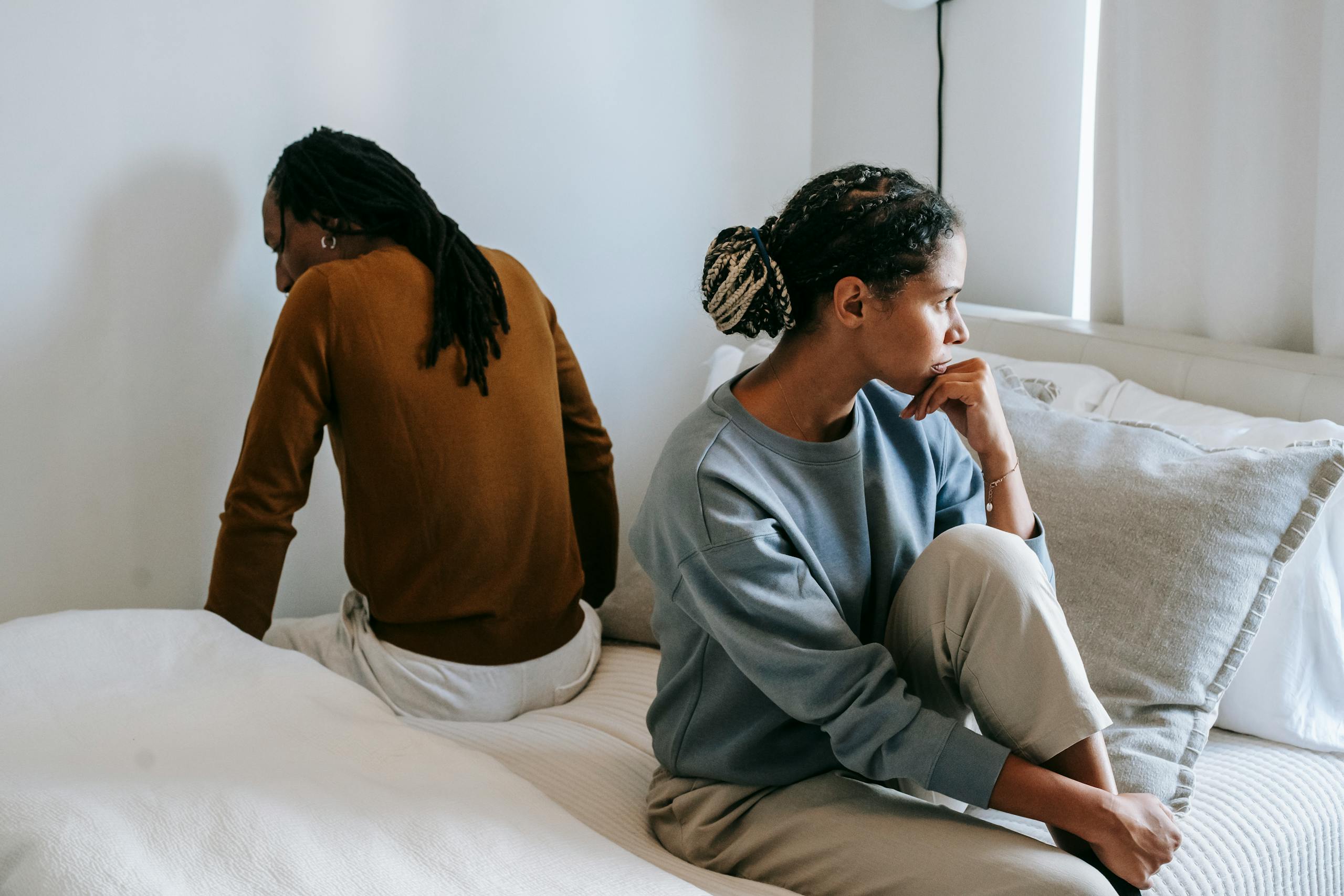 Young discontented African American female touching chin near anonymous male partner during dispute in bedroom