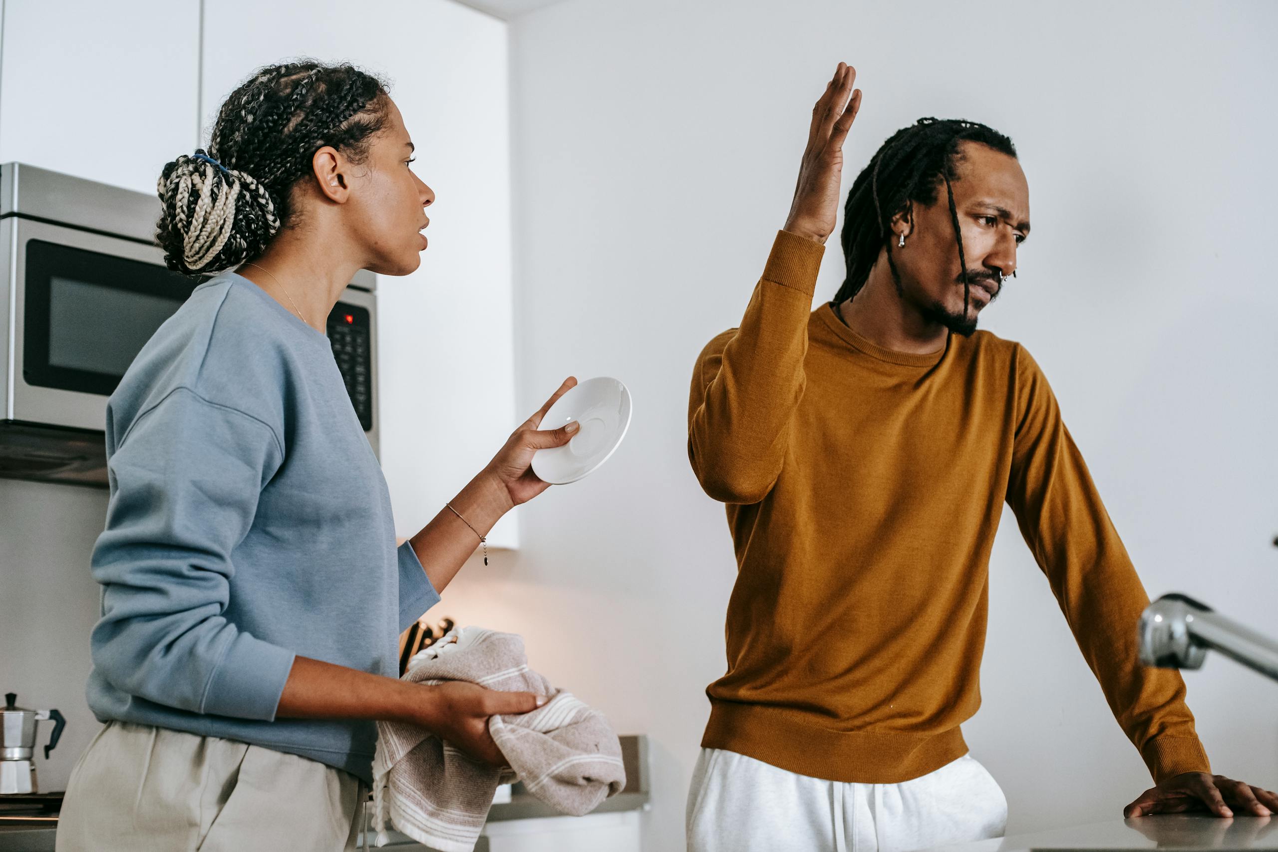 Young dissatisfied African American man with raised arm having conflict with girlfriend in house