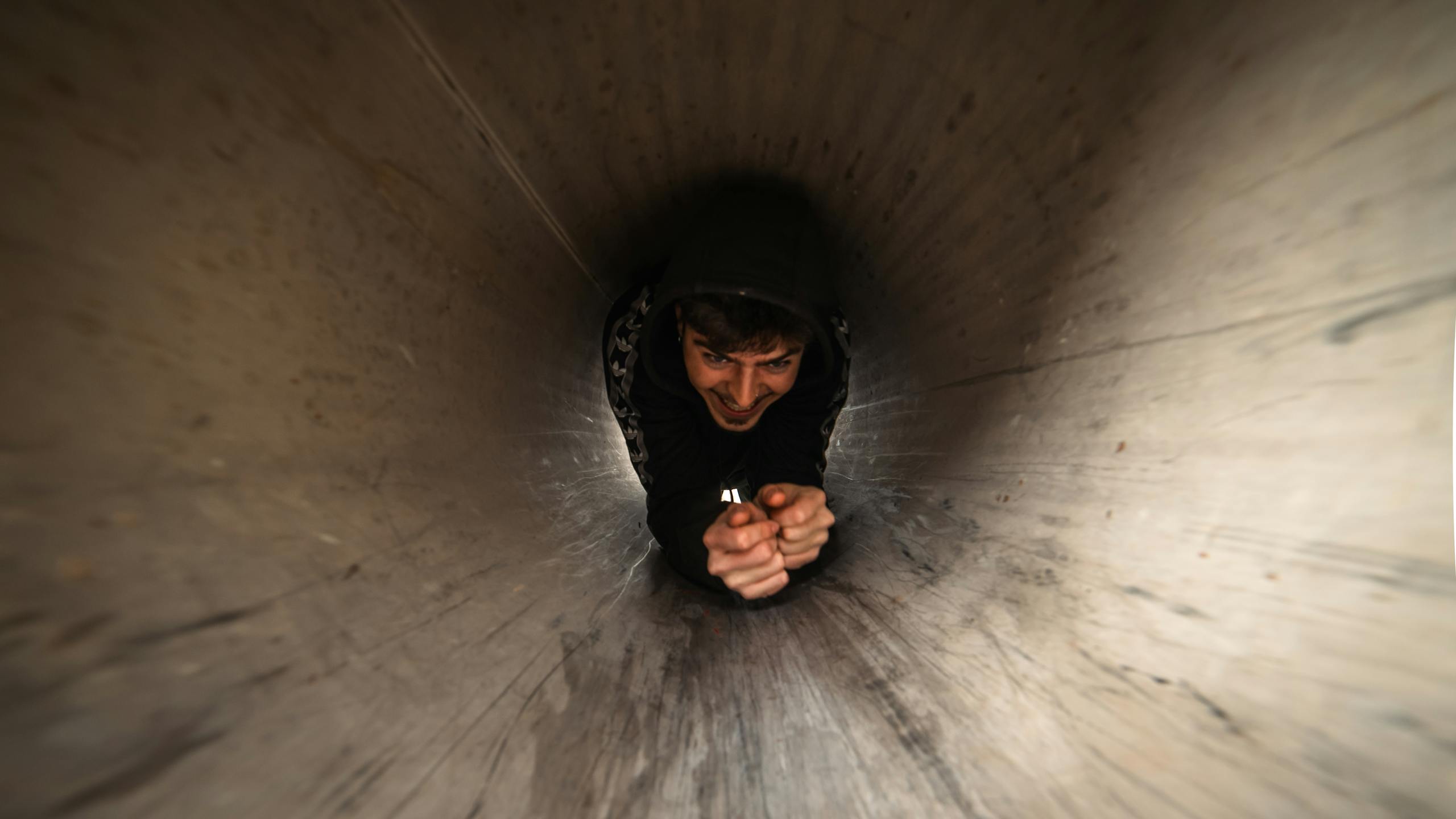 Young man crawling through a dimly lit metal tunnel, capturing a playful and adventurous moment.